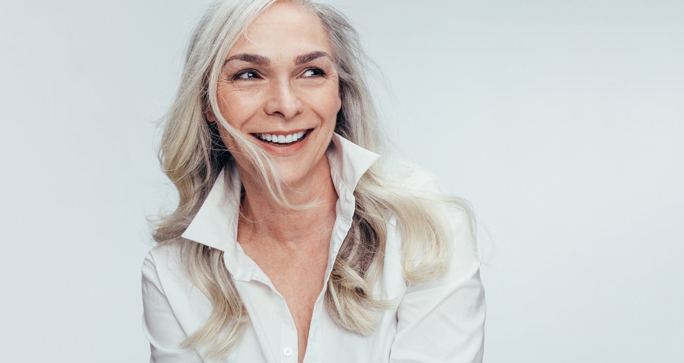 Beuatiful woman in her 60s with long gray hair. She has a popped collar and is smiling while looking away from camera. Her youthful appearance at her age emulate the results one could achieve with a Beverly Hills Facelift with Dr. Torkian