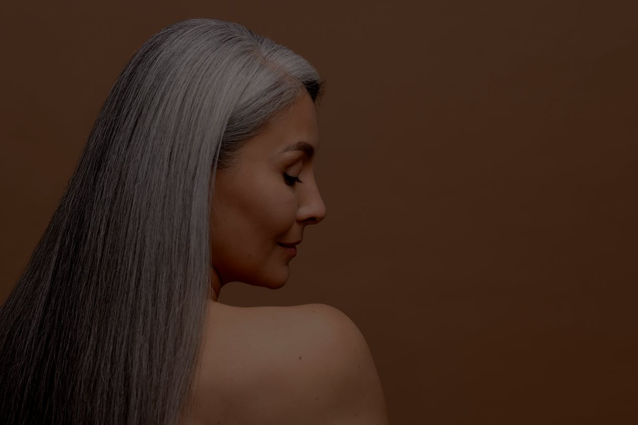 Older woman with gray hair has back to camera and face turned to see her profile in a studio shoot. Her youthful appearance despite her age, shows the potential results of a deep plane facelift in Beverly Hills with Dr. Torkian