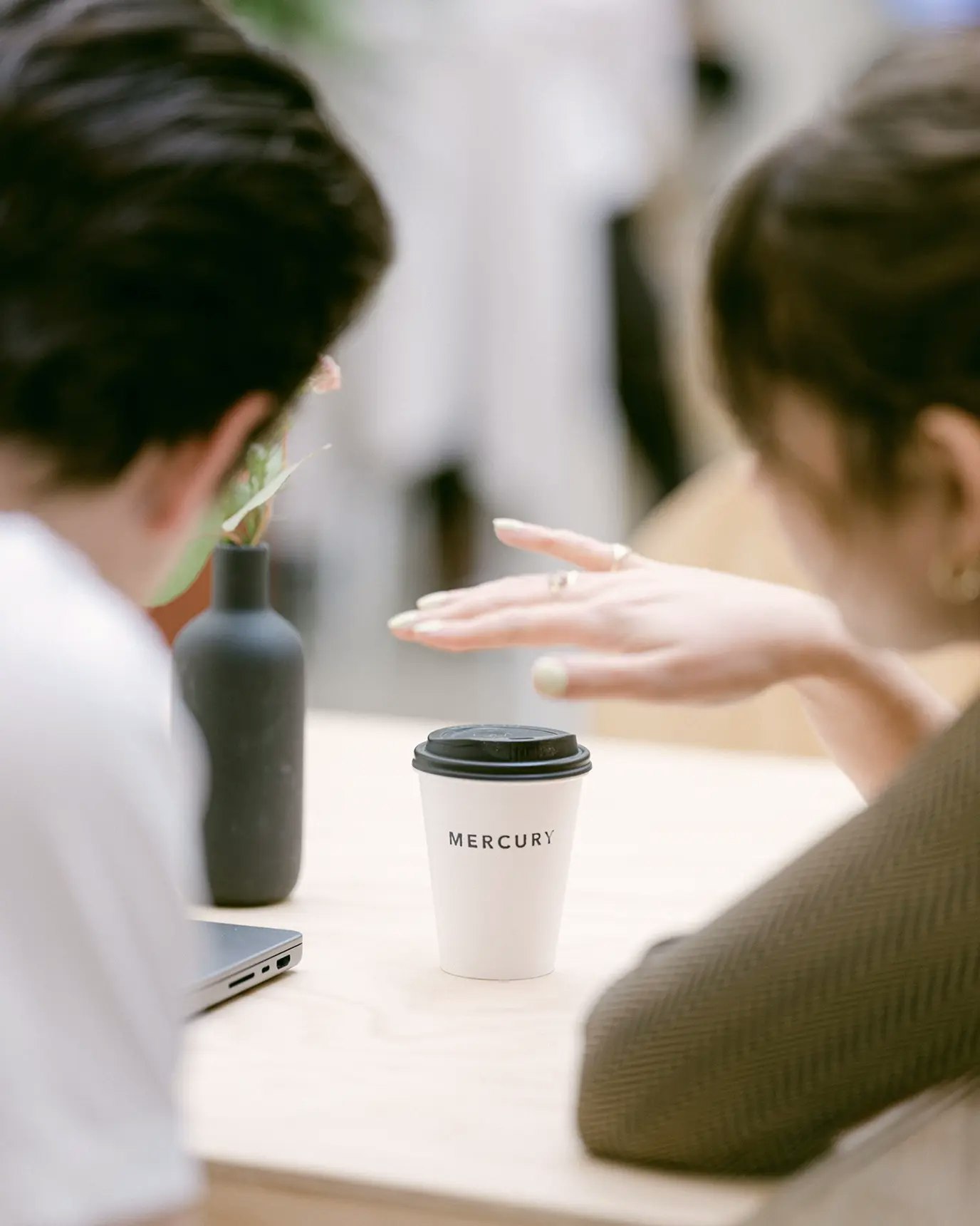 Two attendees in the foreground with a Mercury branded coffee cup in focus