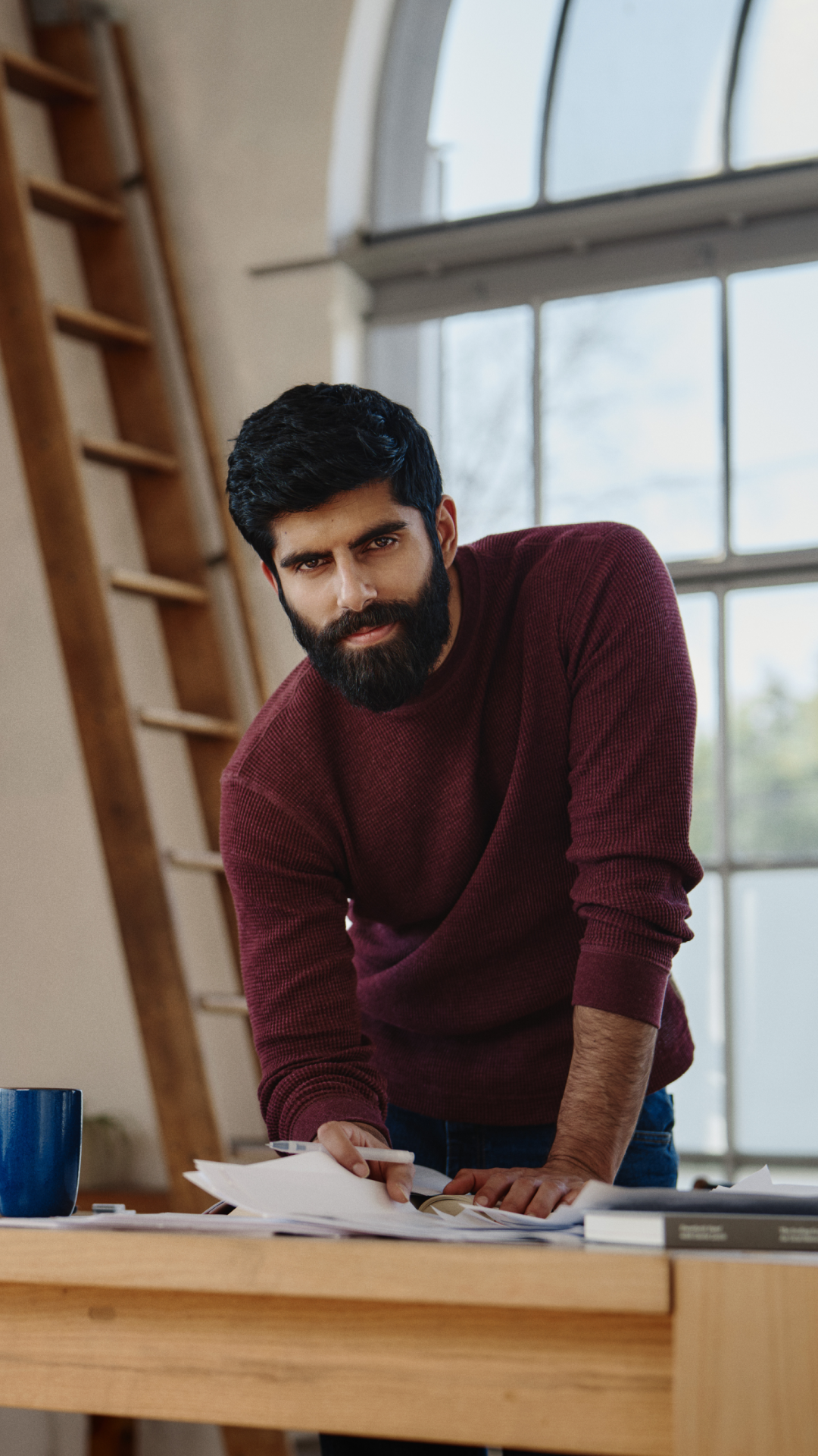 Portrait of a customer, Dwarkesh Patel, in a studio space, at a desk with papers, books, and podcasting equipment nearby.