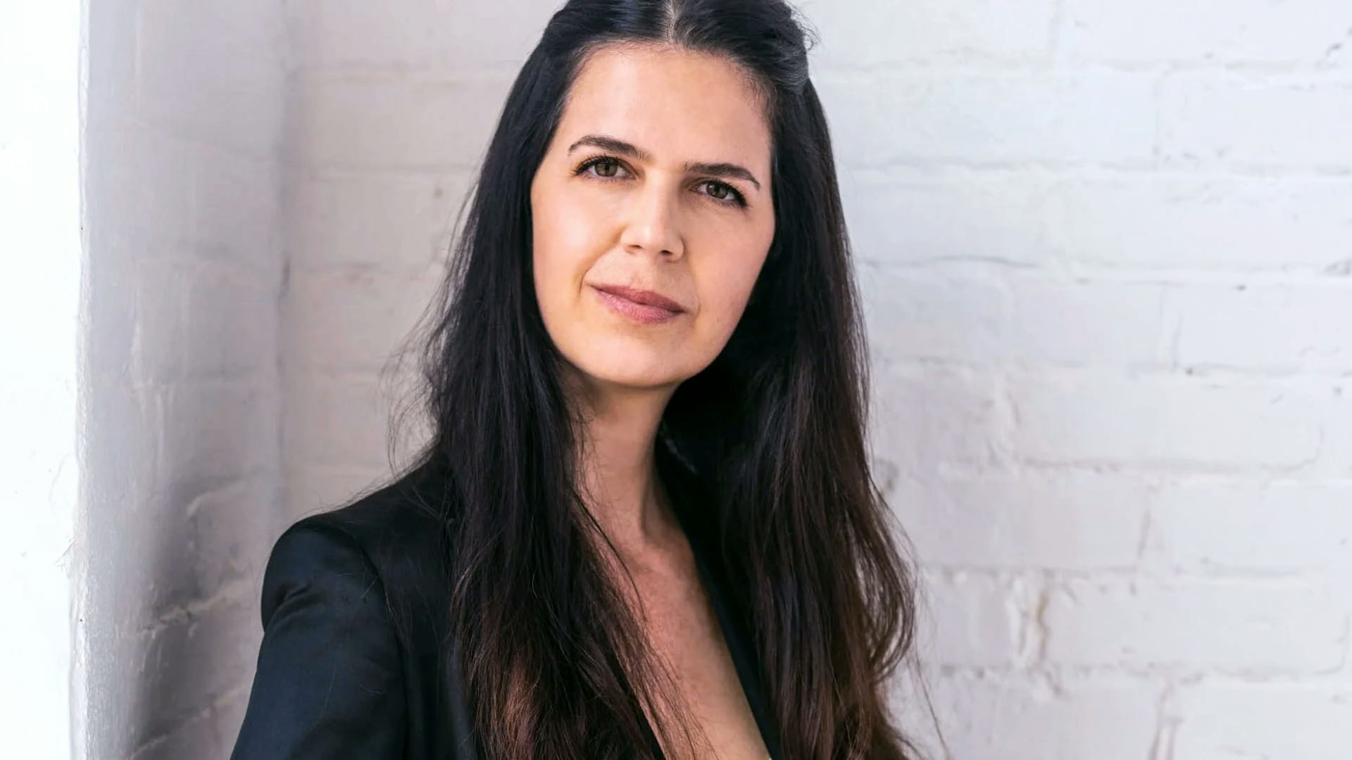 Woman with dark hair wearing a suit jacket looks directly at the camera.