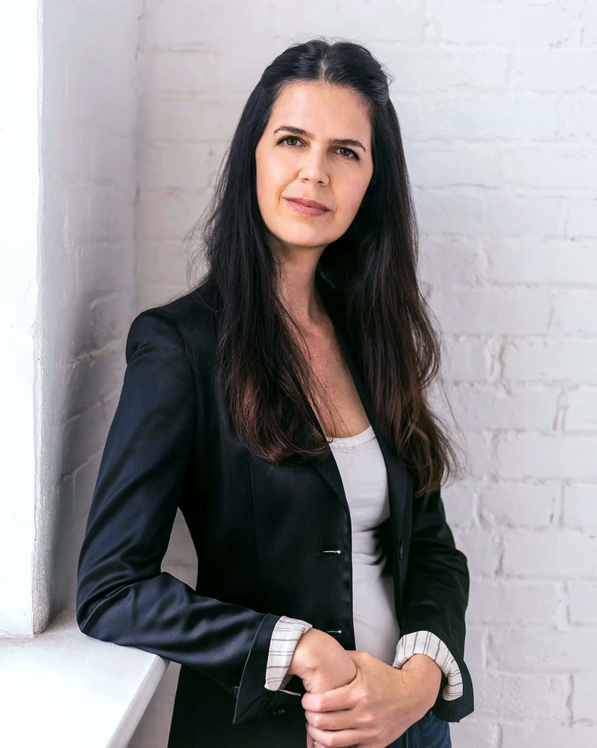 Woman with dark hair wearing a suit jacket looks directly at the camera.
