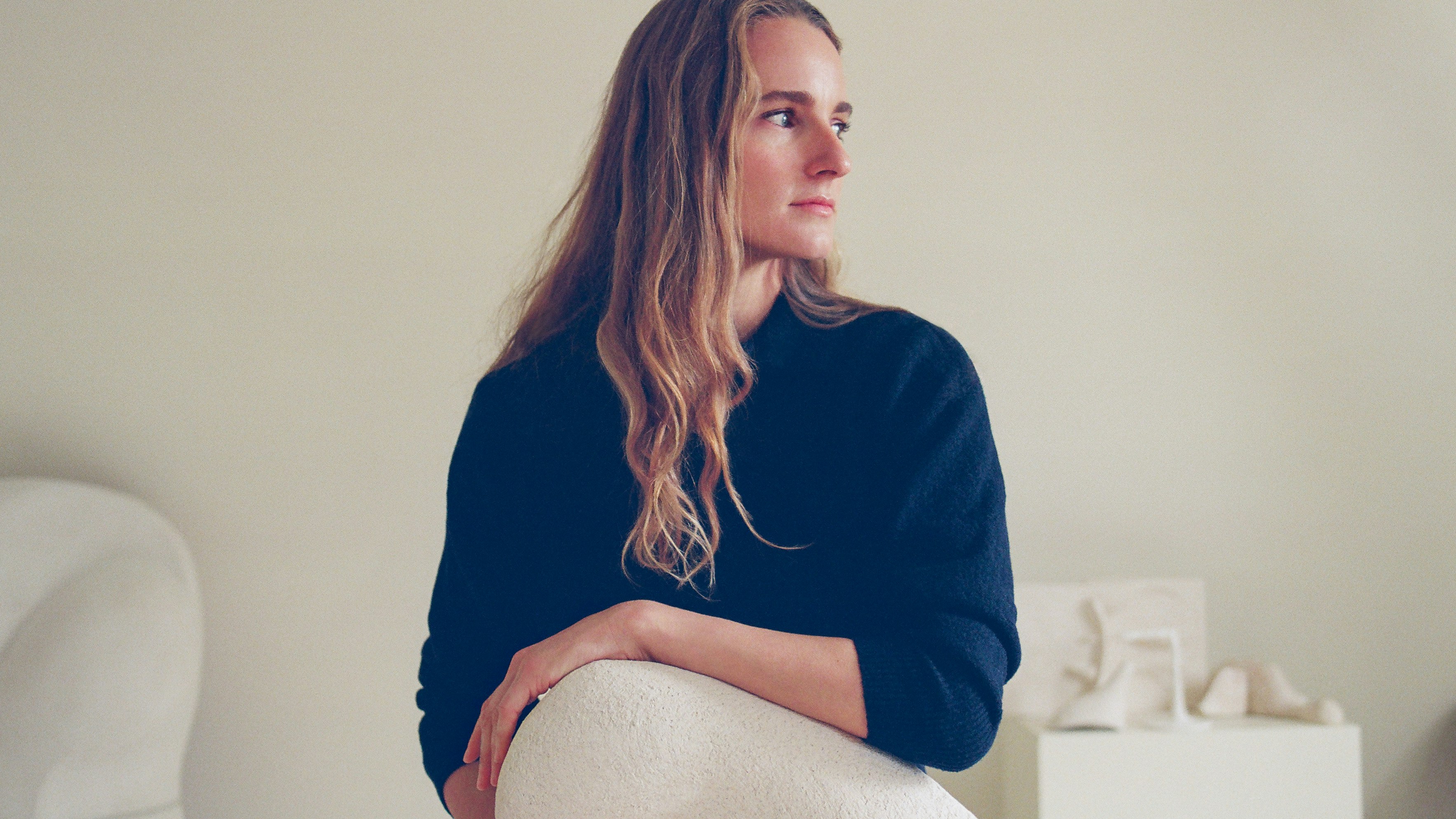 Woman inside an all-white studio space looks to her left while cradling a white sculpture in her hands.