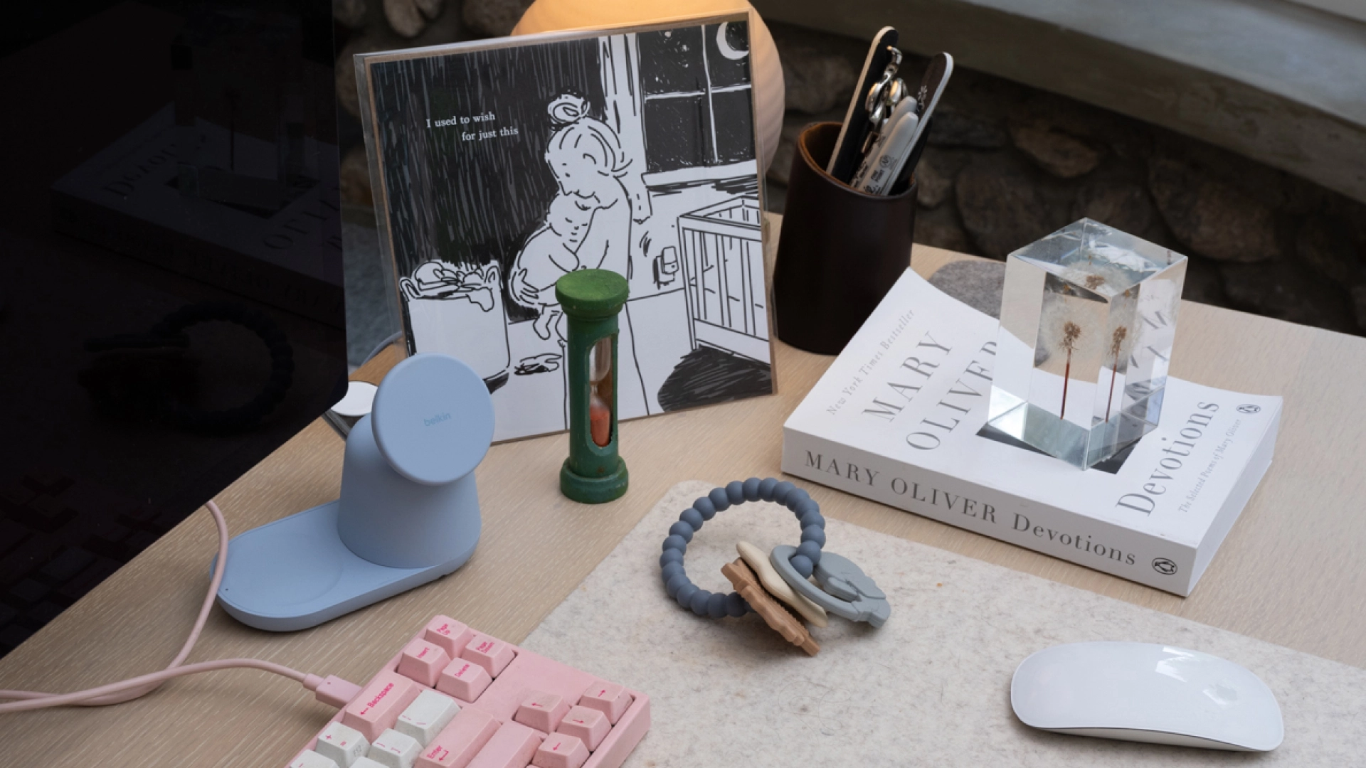 Top of desk which holds baby teething rings, a pink keyboard, computer mouse, hourglass, and print.