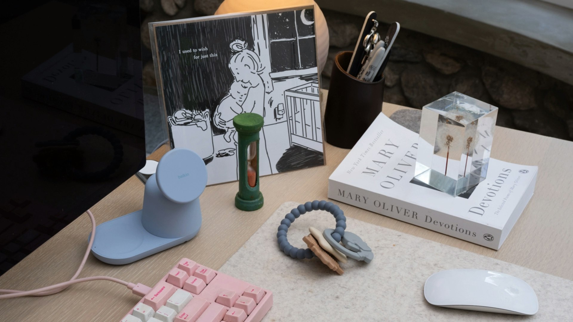 Top of desk which holds baby teething rings, a pink keyboard, computer mouse, hourglass, and print.