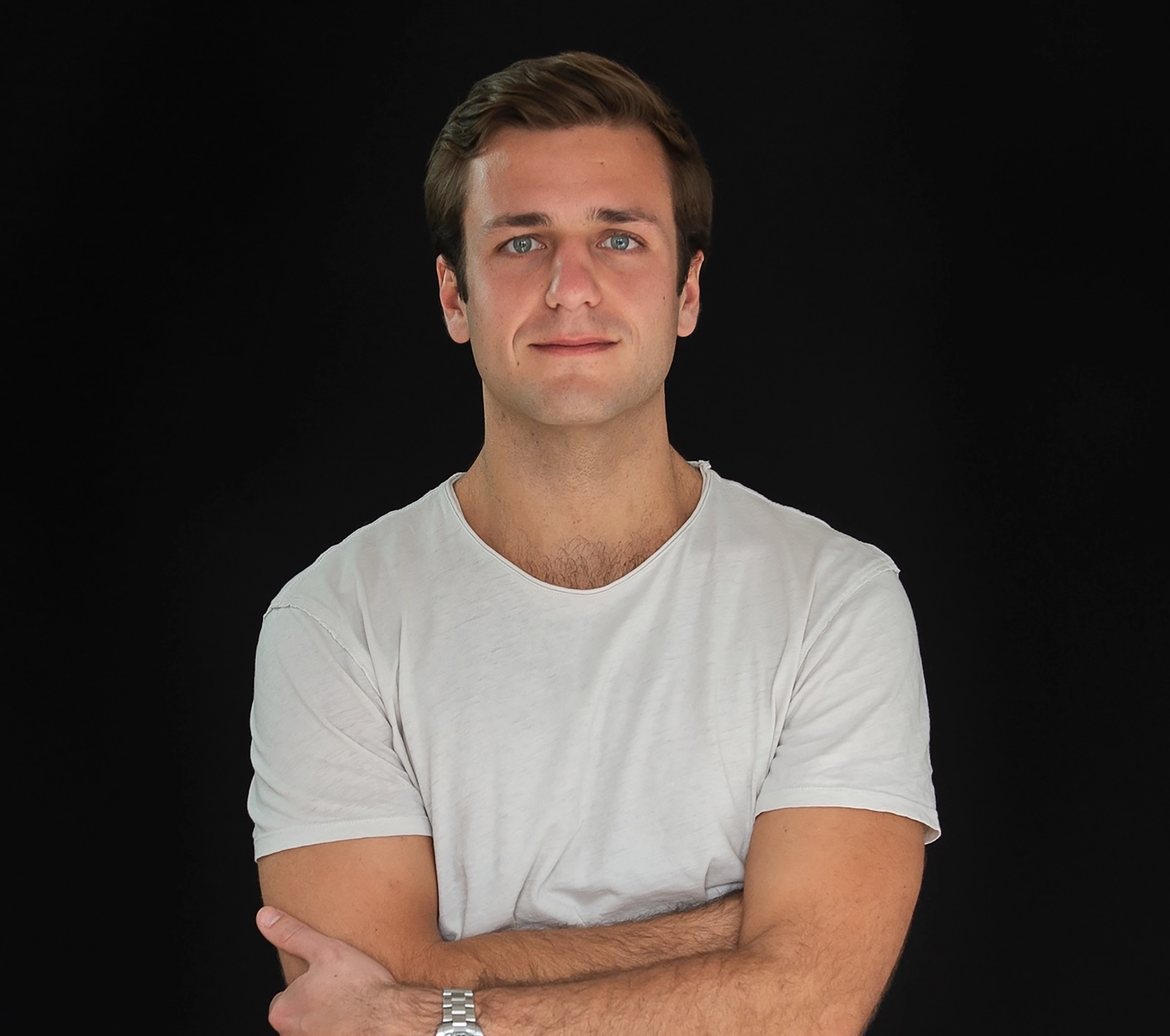 Man wearing white T-shirt and crossing his arms looks directly at the viewer.