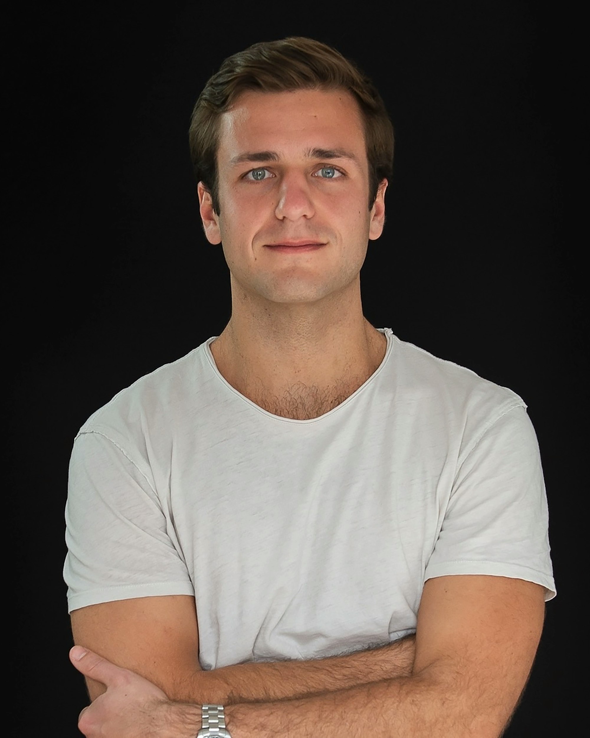 Man wearing white T-shirt and crossing his arms looks directly at the viewer.