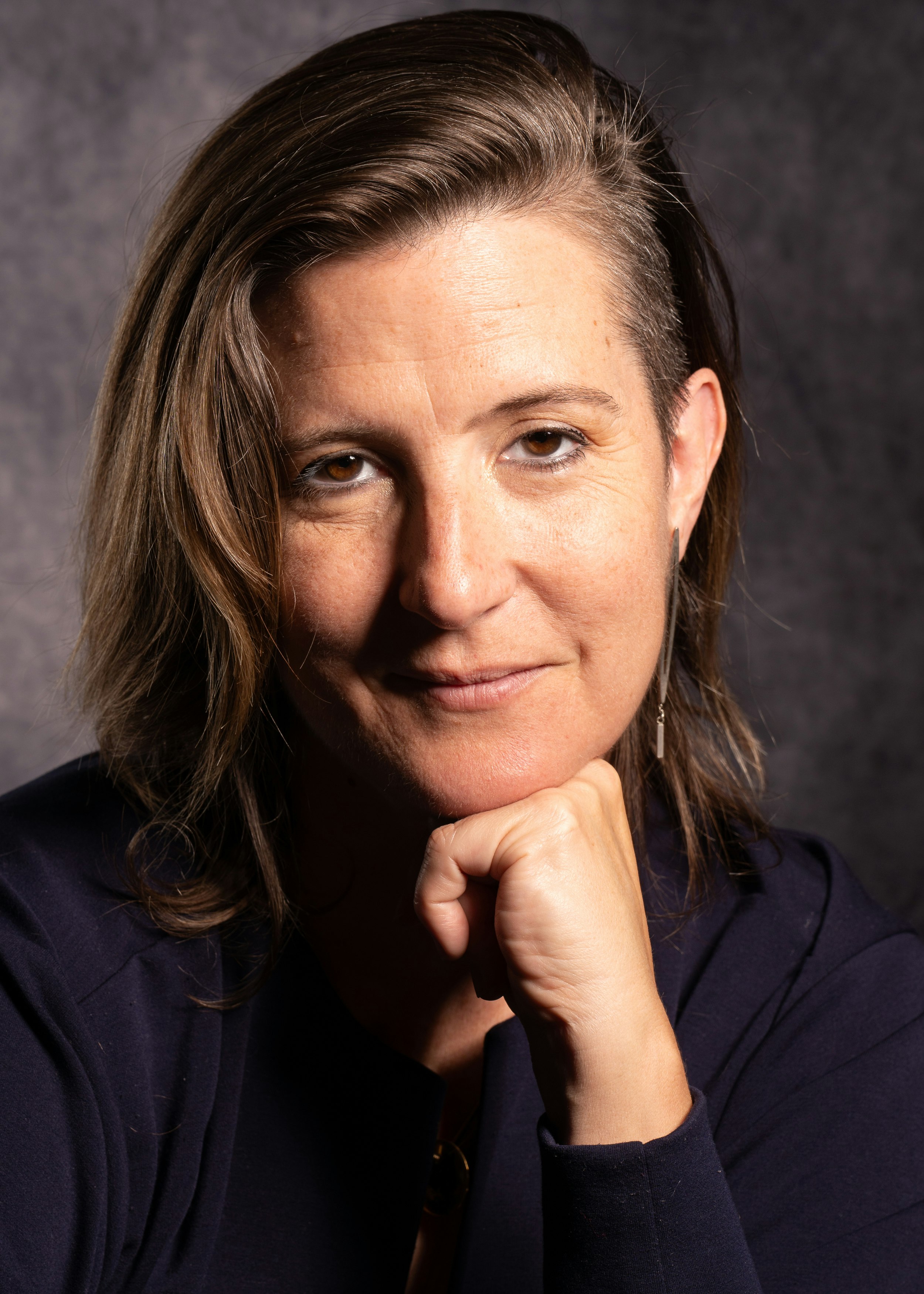 Woman wearing black turtleneck resting her chin on her closed fist looks directly at the camera.