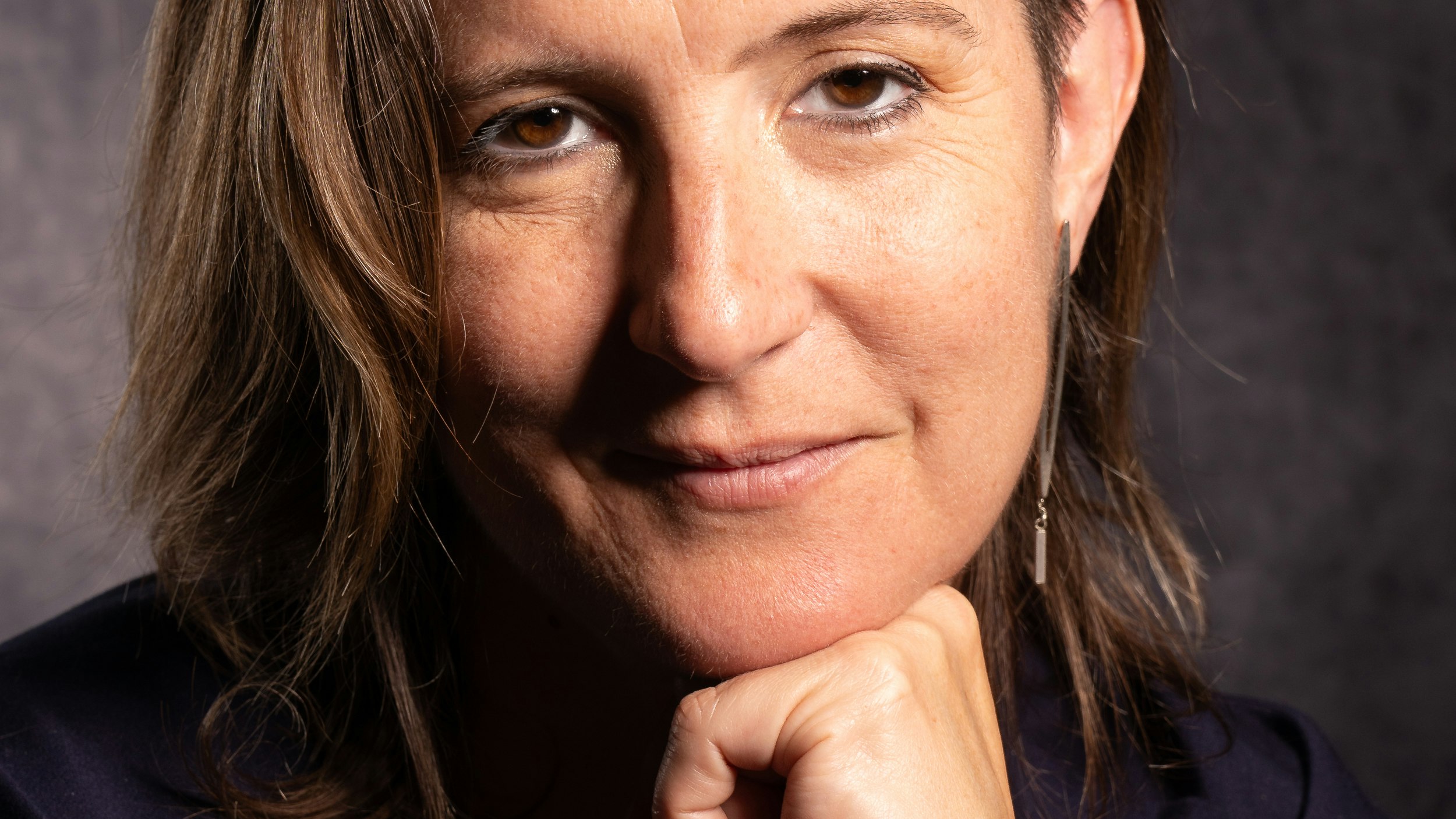 Woman wearing black turtleneck resting her chin on her closed fist looks directly at the camera.