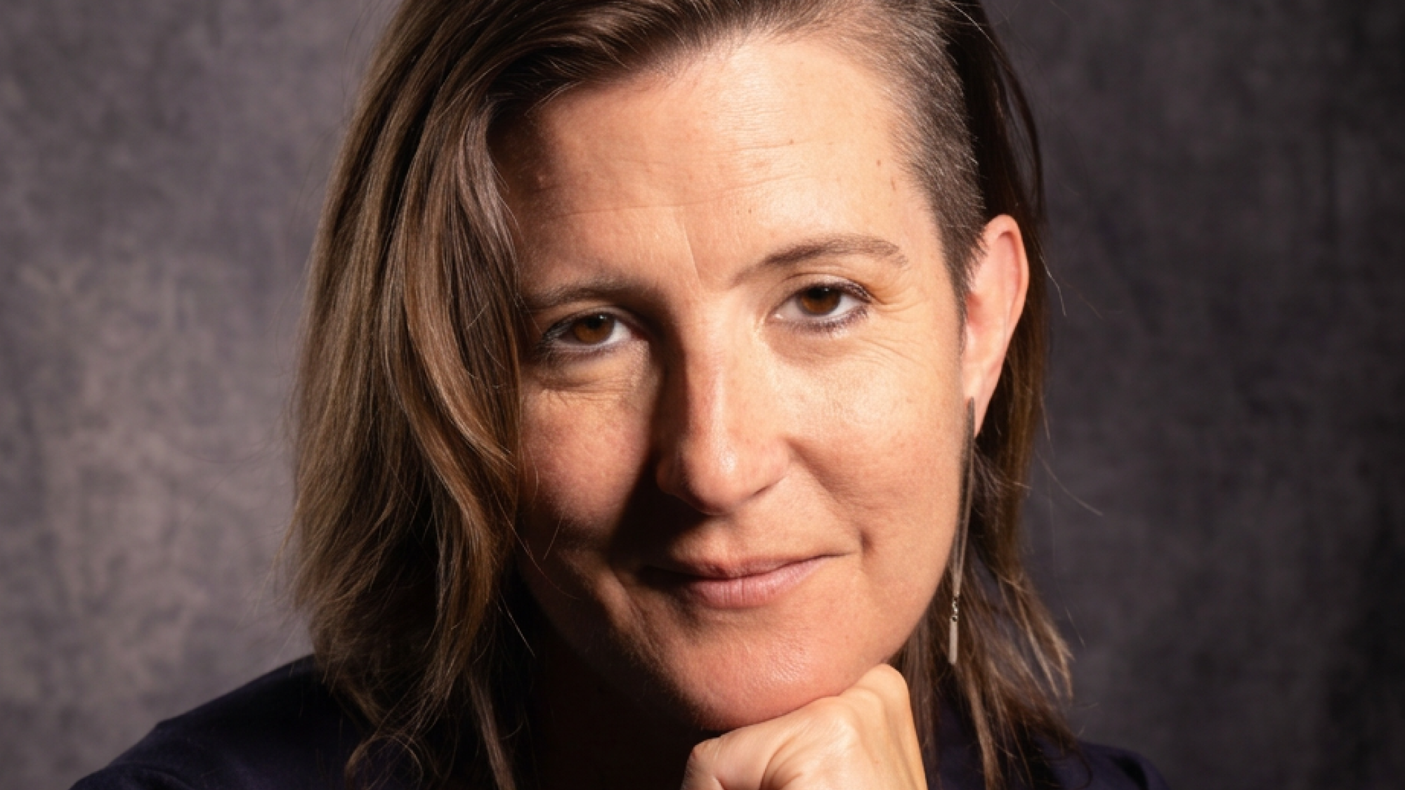 Woman wearing black shirt rests her chin on her hand while looking directly at the camera.
