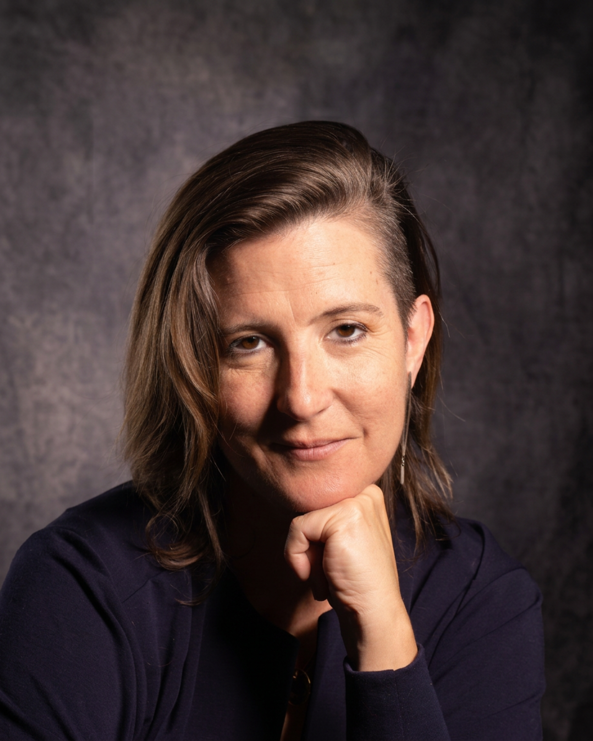 Woman wearing black shirt rests her chin on her hand while looking directly at the camera.
