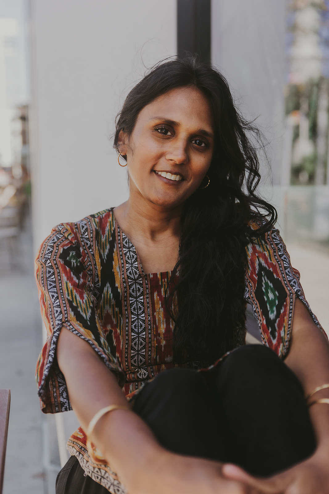 Woman with long hair and colorful print top smiles at the camera.