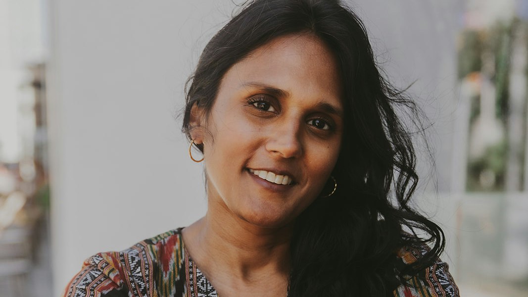 Woman with long hair and colorful print top smiles at the camera.
