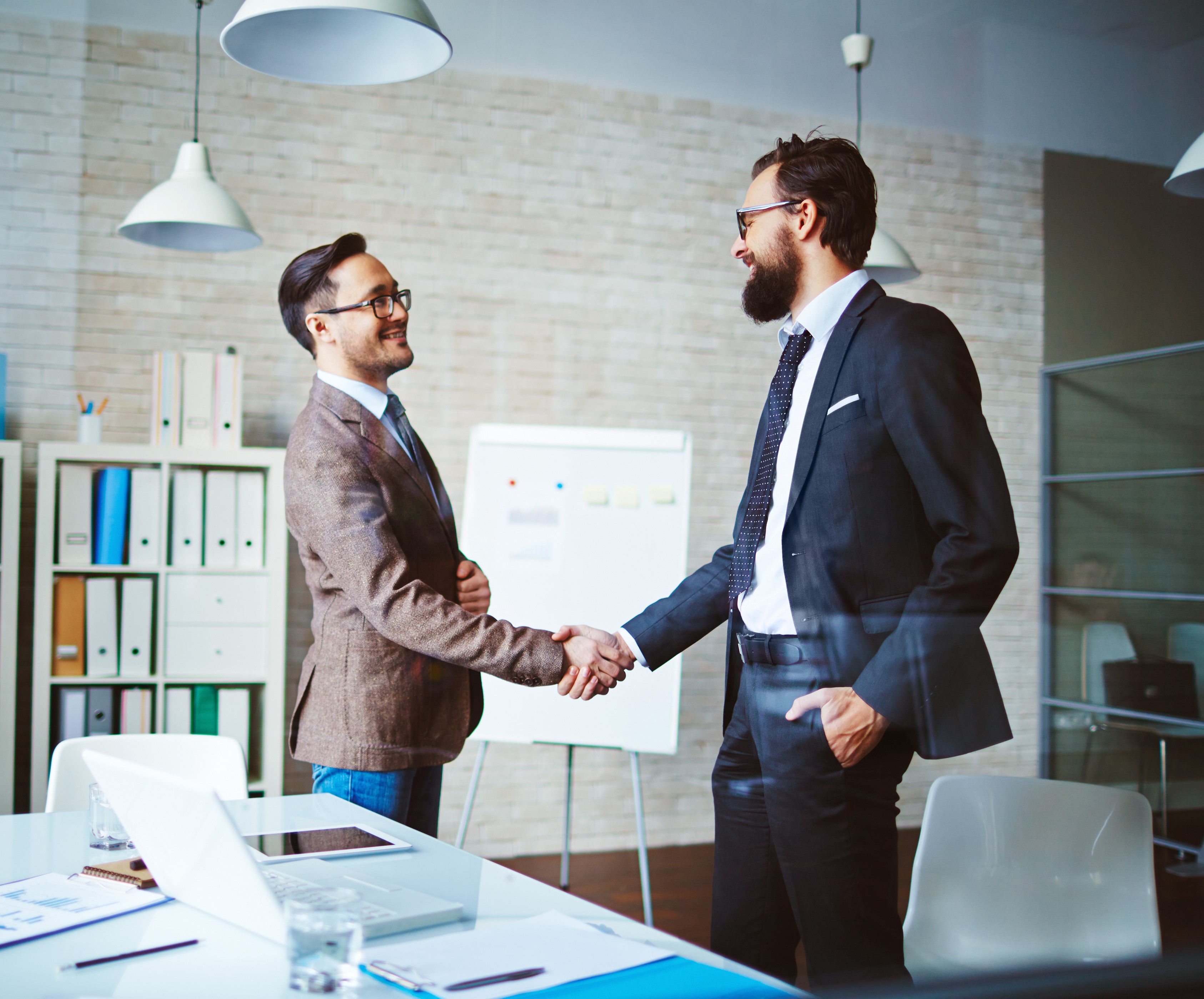 Two men are shaking hands and smiling to each other.