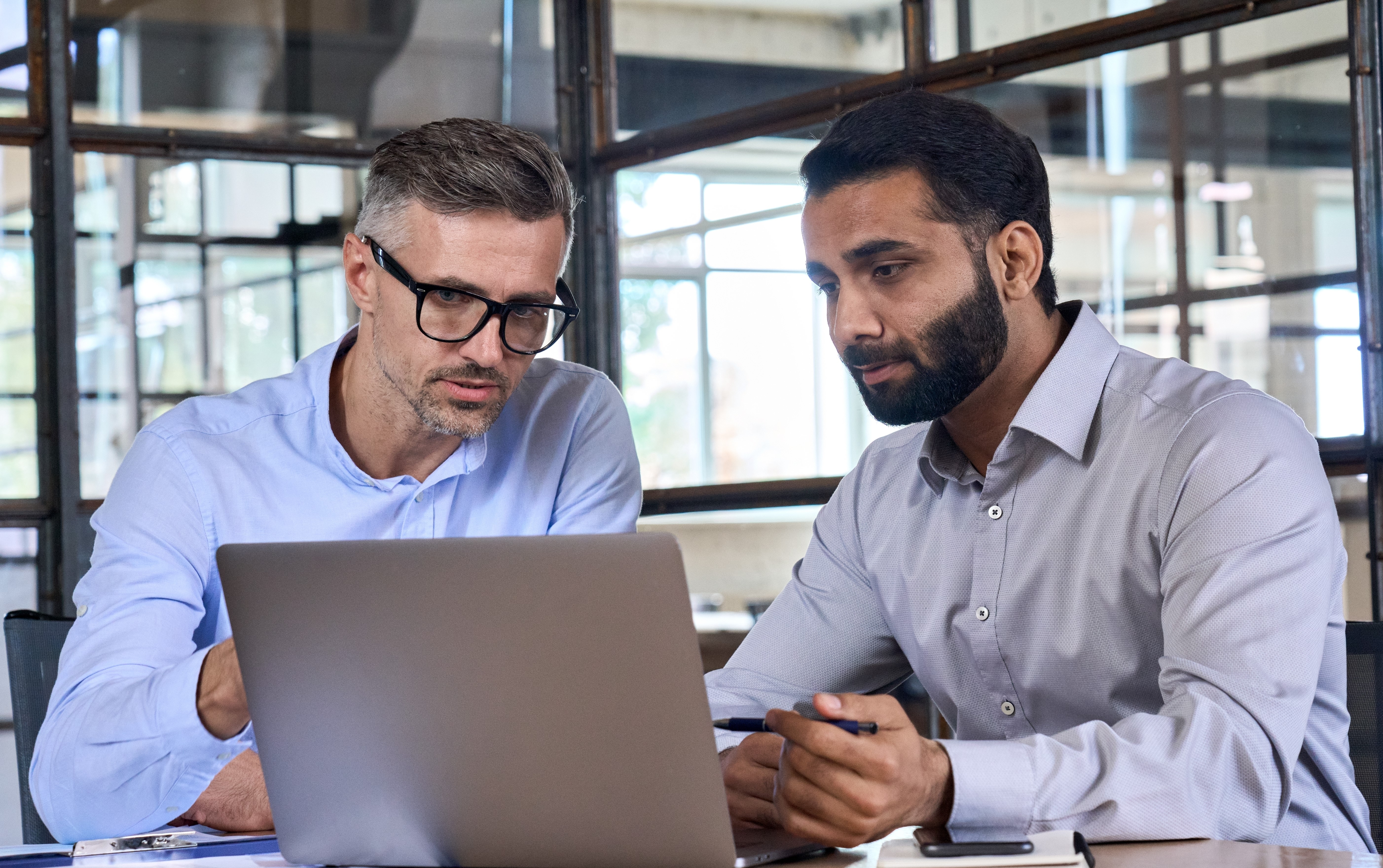 Two men are sitting near the laptop and discussing something.