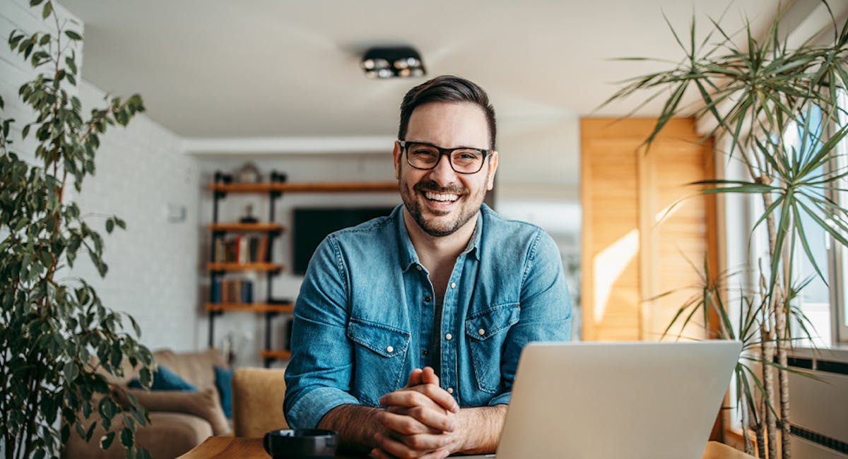 man sitting at breakfast table with laptop smiling