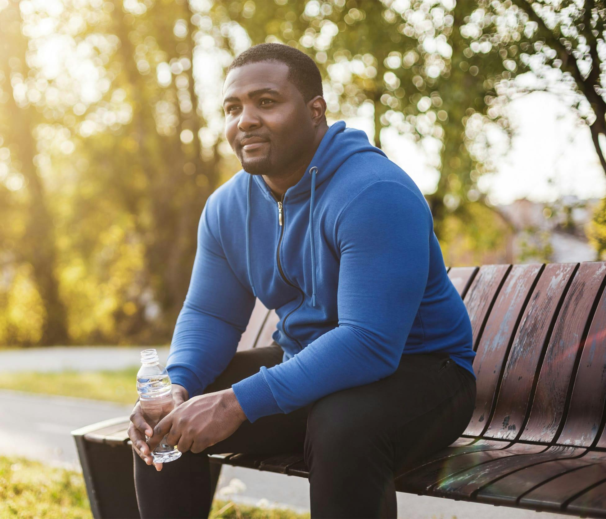 Man smiling and sitting on park bench holding bottle of water