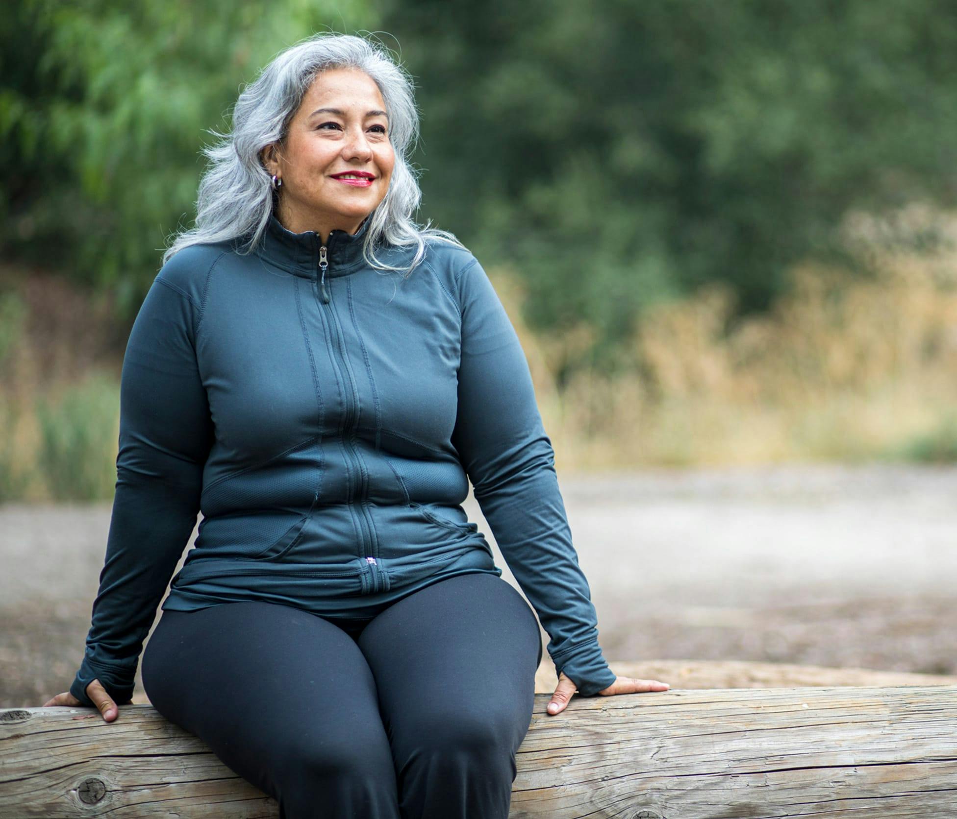 Woman smiling and sitting on log outside