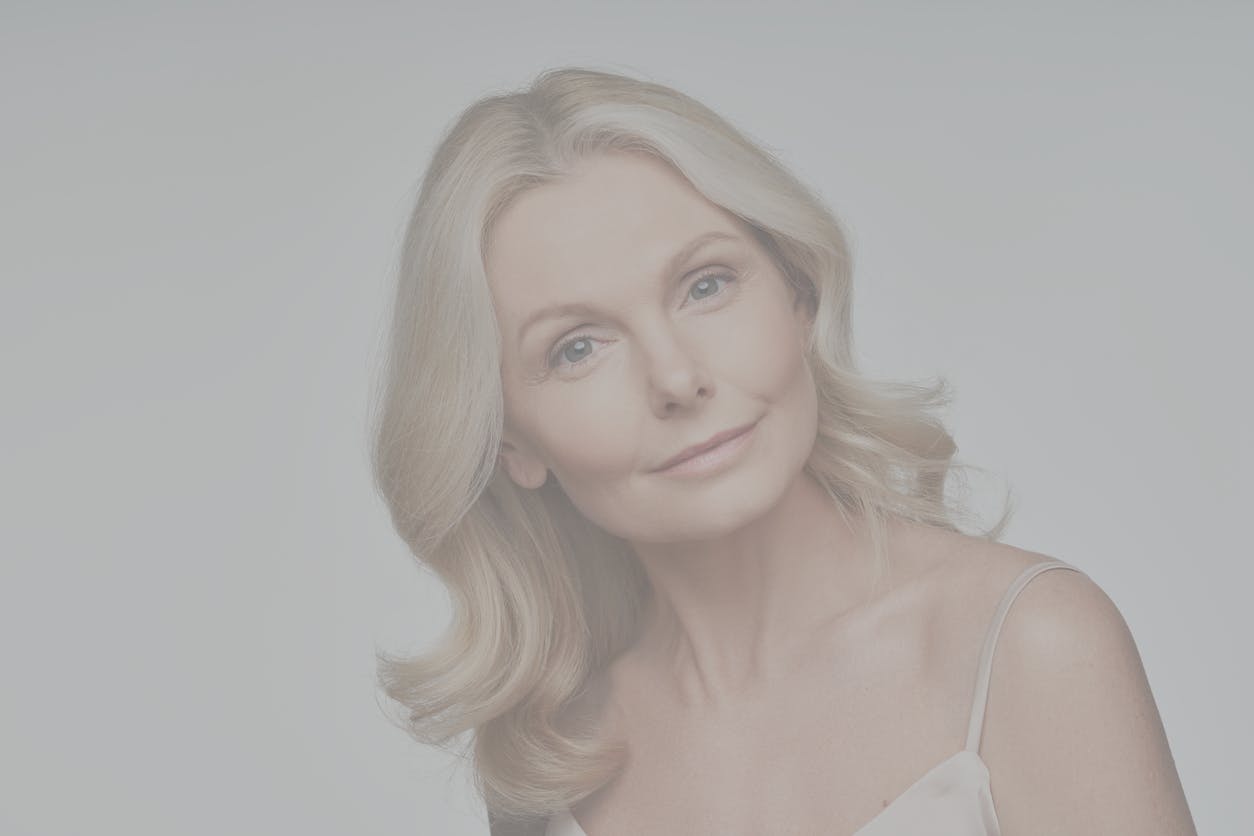 Older woman with blonde hair smiles at the camera in a studio shoot. Her youthful beauty even at her age emulates the potential results of a facelift in Frisco, Plano, Allen, and McKinney