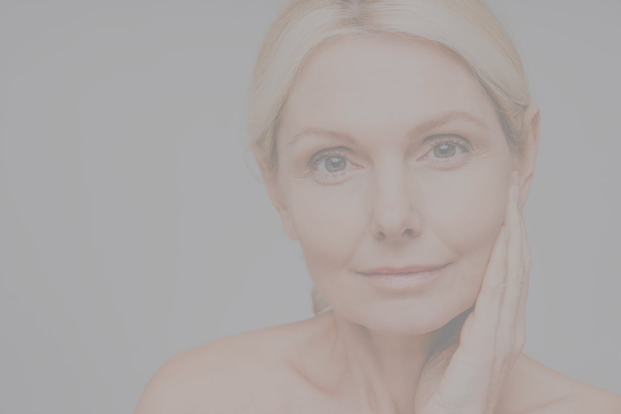Older woman with blode hair tied back looks at the camera with a small smile. Her youthful eyes show the potentail results of a blepharoplasty in McKinney
