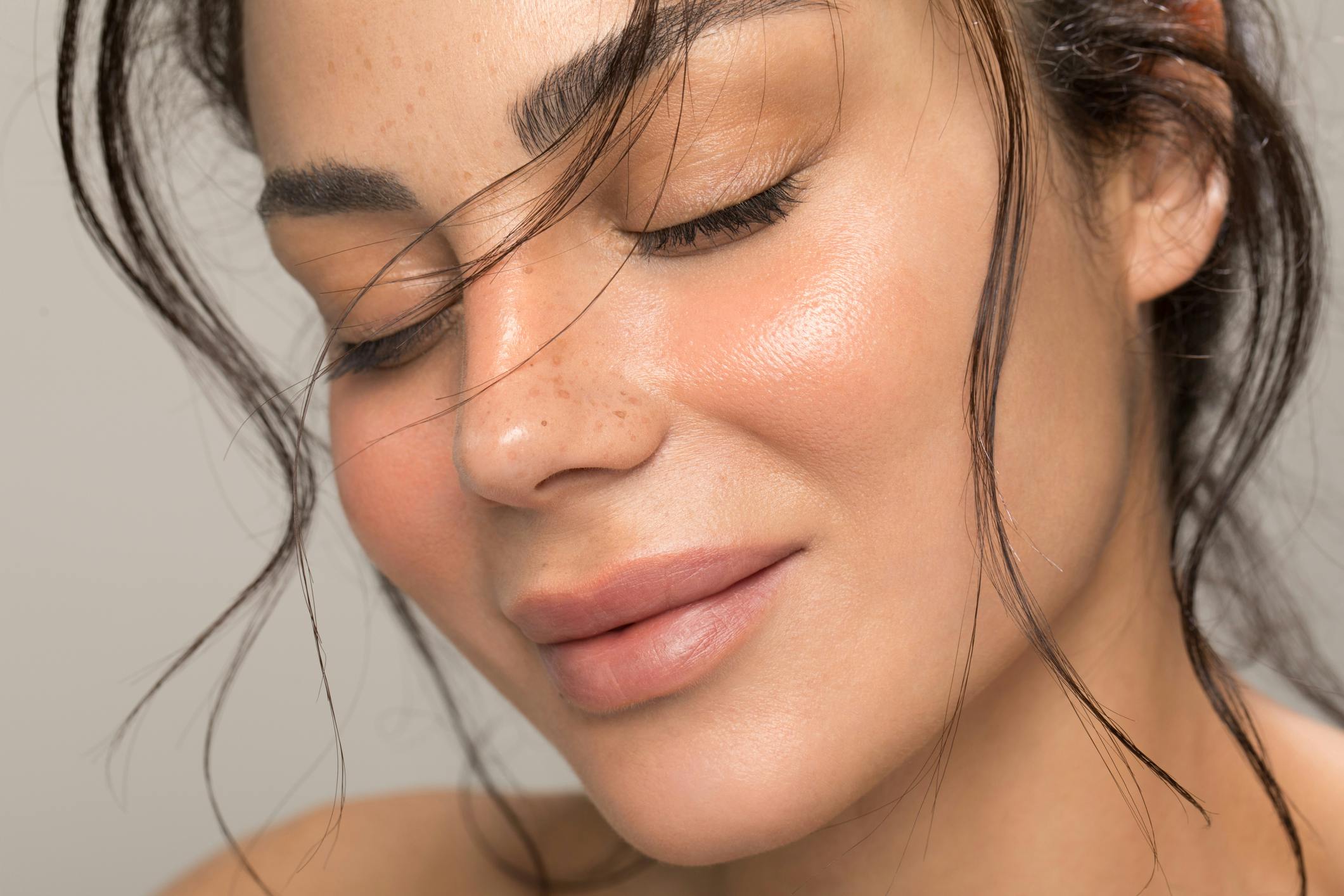 Young woman with hair flowing in her face has eyes closed and smiling in a studio shoot. Her symmetrical ears show the potential results of ear surgery in McKinney