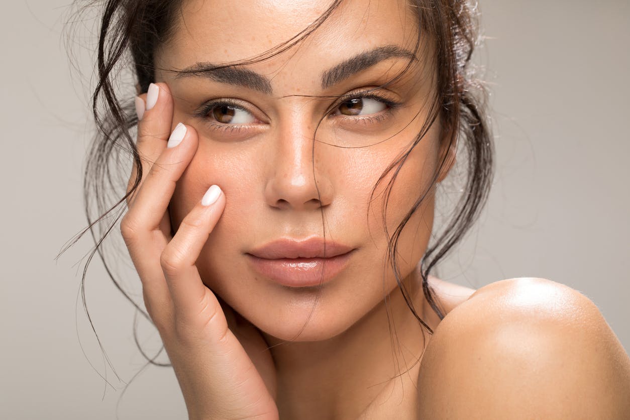 Woman looking seductively away from the camera as her hand rests against her cheek. Her eyebrows are raised to show the potential results of a brow lift in McKinney