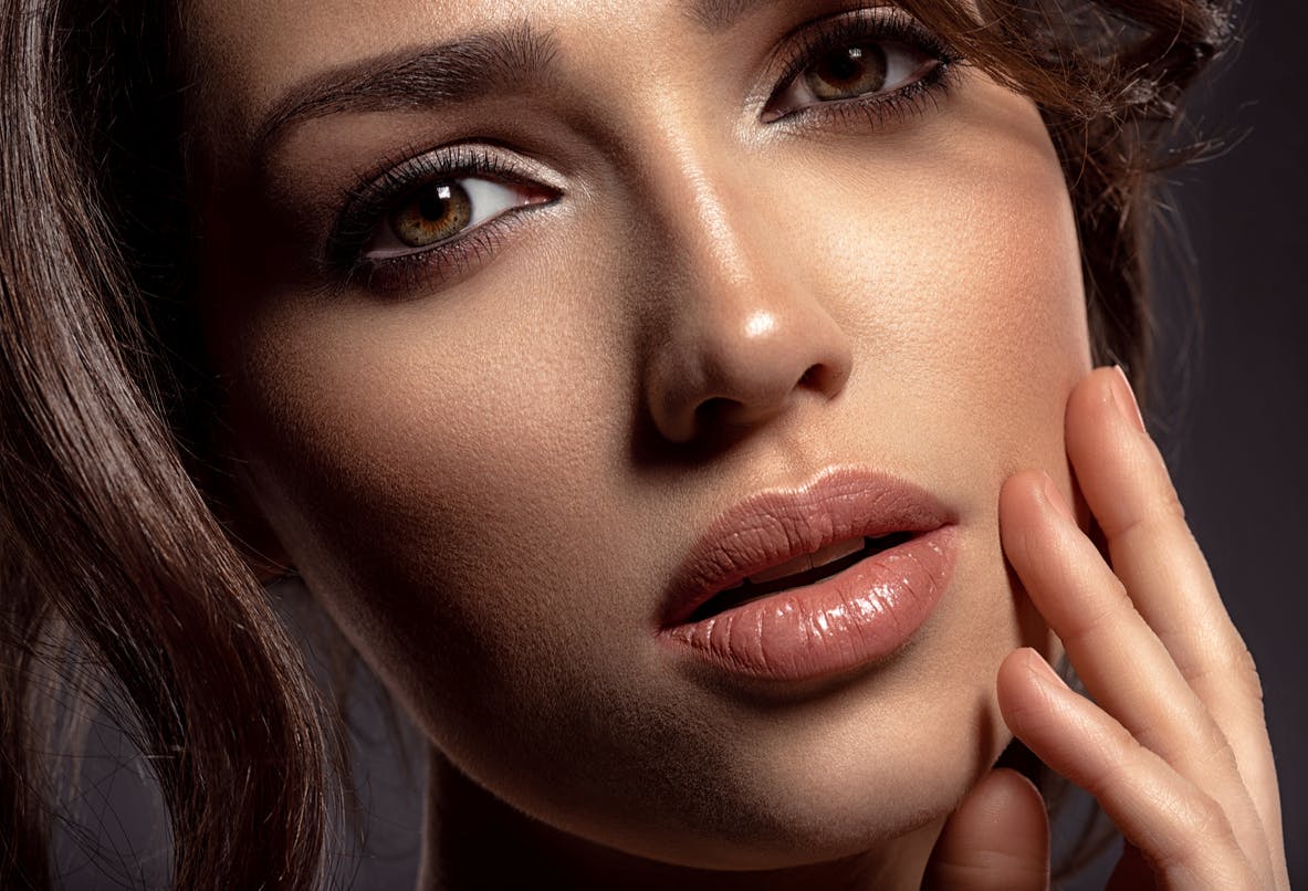 Woman looking seductively away from the camera as her hand rests against her cheek. Her symmetrical face is to show the potential results of a chin augmentationin McKinney