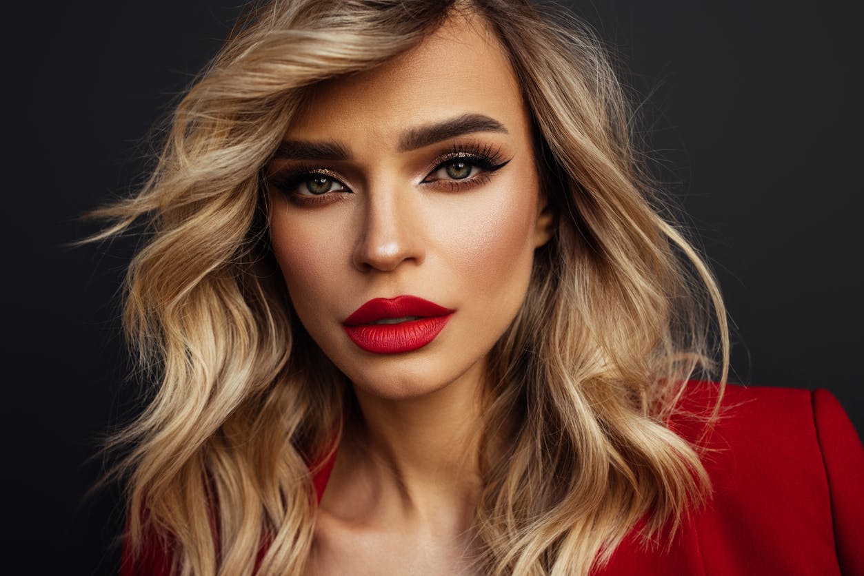Woman with full makeup done and long blonde hair looks intensely into the camera. She has bright red lopstick on and her defined cheeks and chin show the potential results of buccal fat removal in McKinney with Setty Plastics and Aesthetics