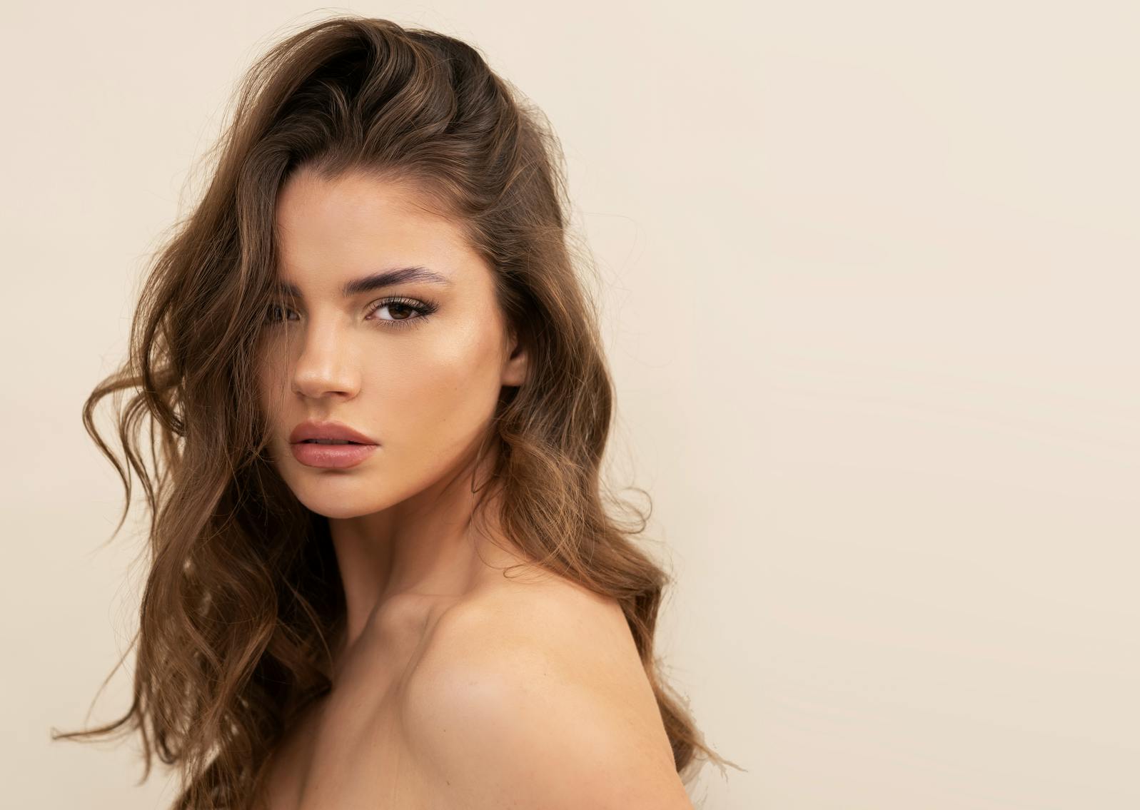 Woman with full makeup done and long brown hair looks intensely into the camera. Her defined cheeks and chin show the potential results of buccal fat removal in McKinney with Setty Plastics and Aesthetics