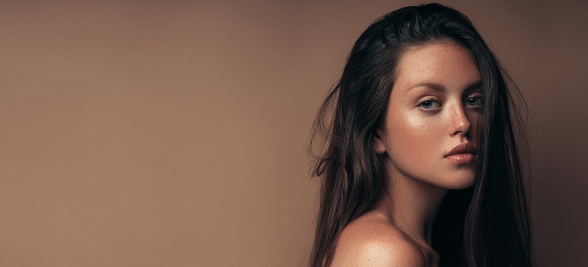 Young woman with full makeup done and long brown hair looks intensely into the camera. Her defined cheeks and chin show the potential results of a fat transfer in McKinney with Setty Plastics and Aesthetics