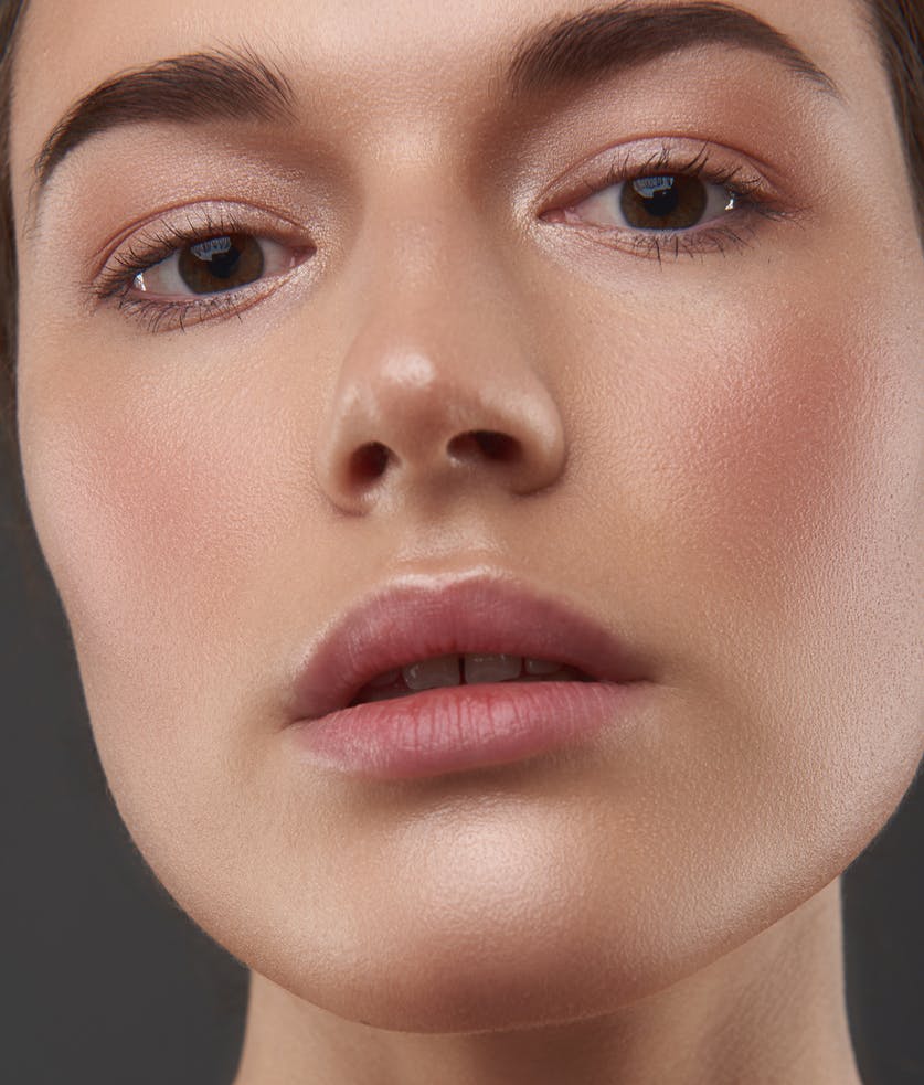 Young woman with brown hair looks at camera in studio shoot. Her glowing skin emulate the potential results of skin resurfacing with laser or chemical peel in McKinney