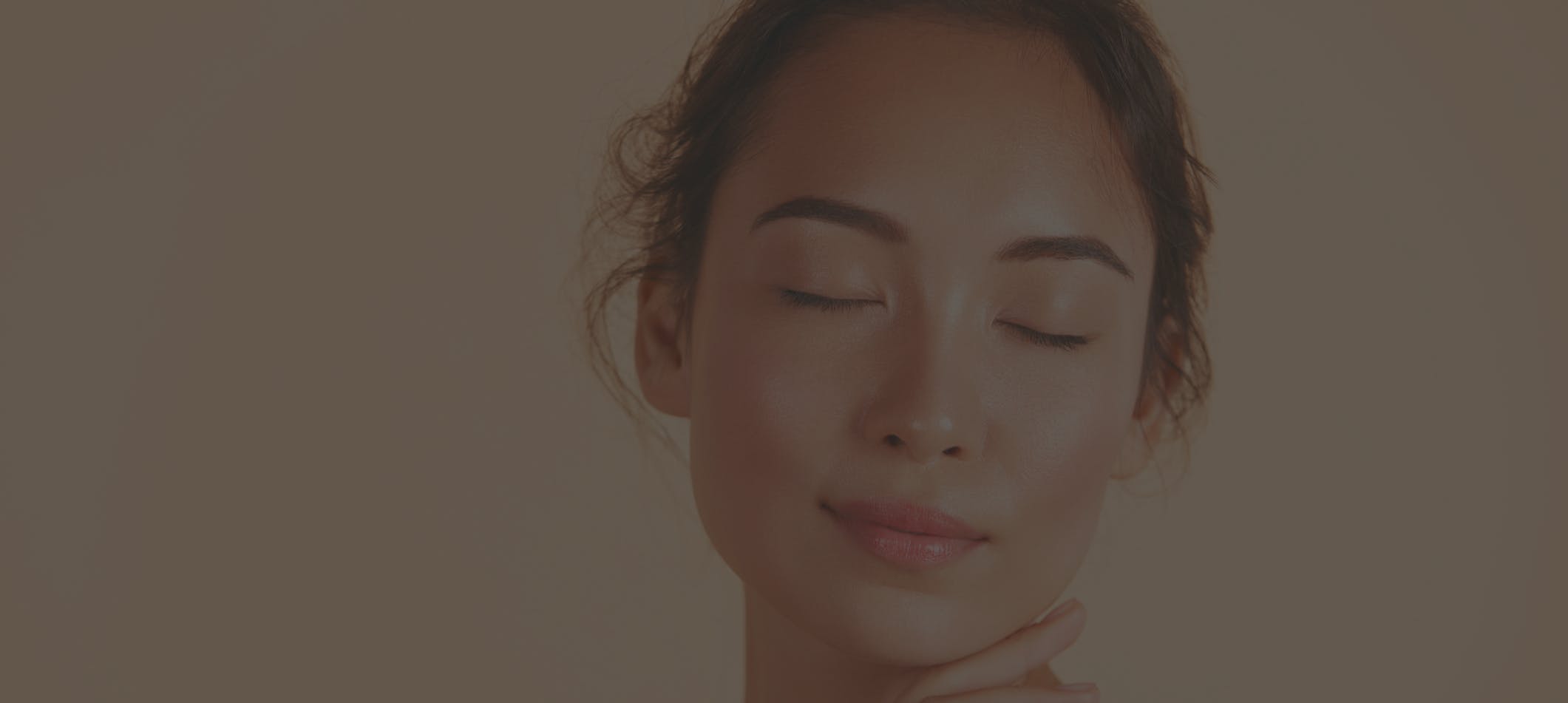 beautiful young woman with smooth skin smiles at the camera with eyes closed and hand at chin. Her glowing skin emulate the potential results of SkinPen® Microneedling