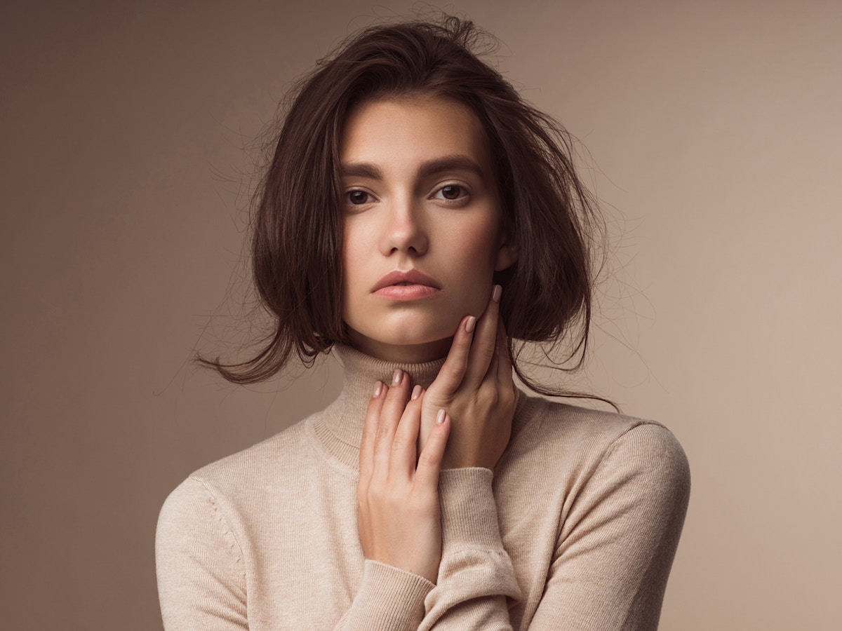 Woman in her 20's is having her portrait taken. Her hair is tucked into her turtlebeck and her hands are by her face. Her wrinkle free face is to emulate the potential results of Dysport in Orlando FL.