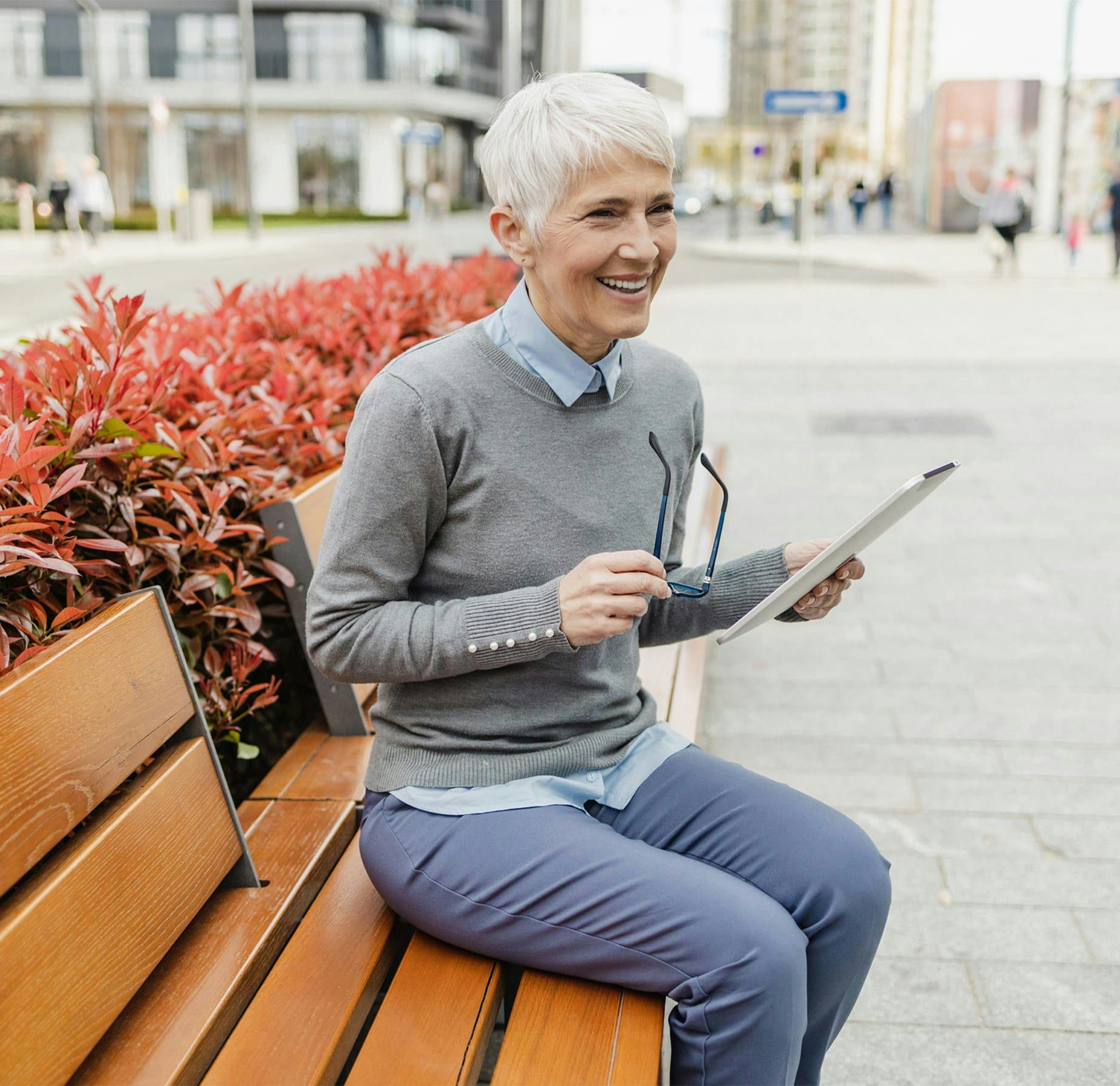 older woman sitting on a bench holding a tablet