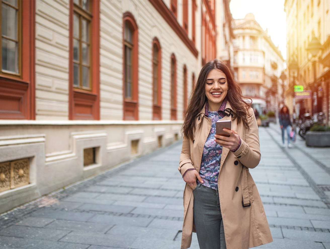 woman smiling at her phone, walking down the sidewalk