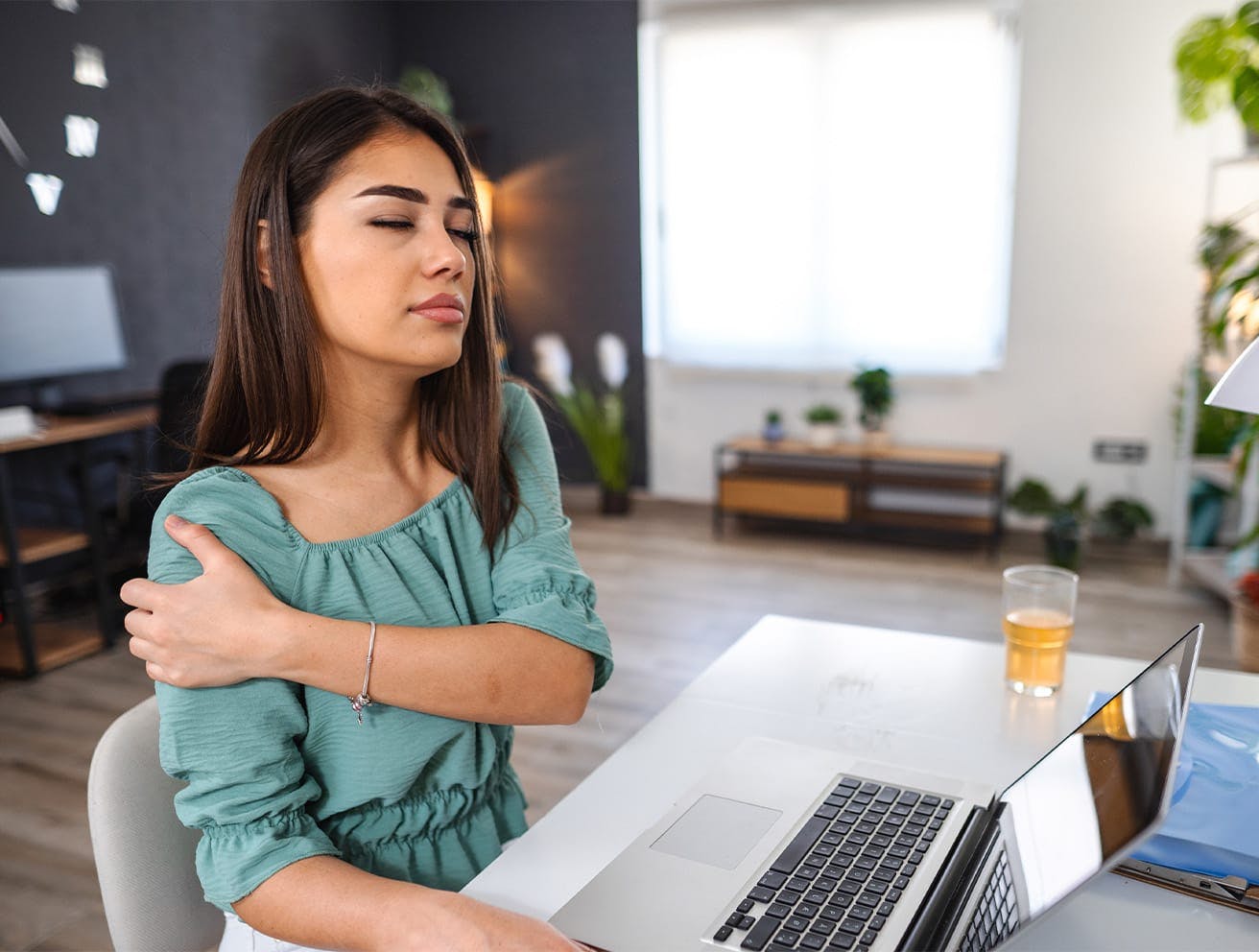 woman sitting at a laptop holding her shoulder