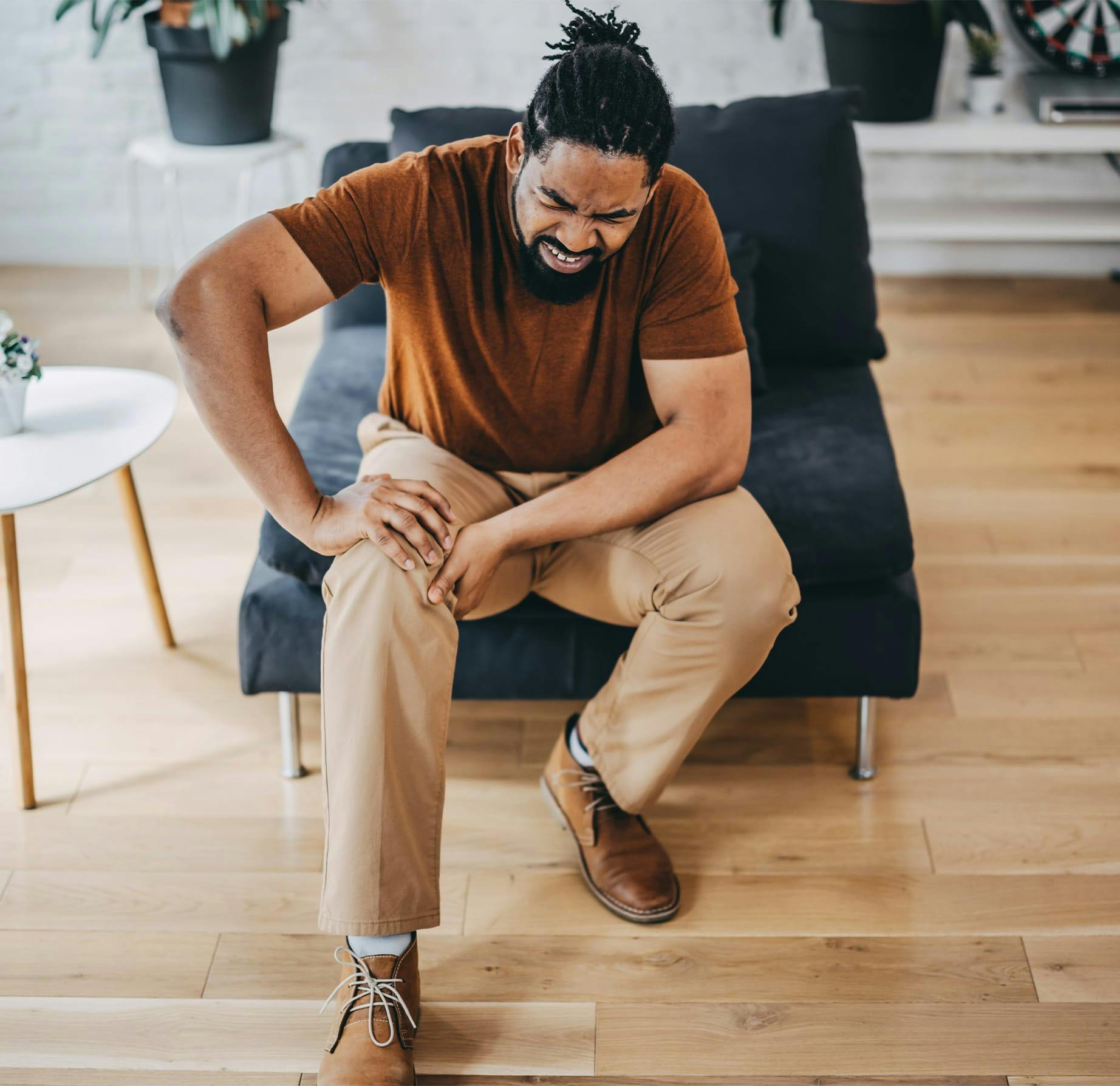 man sitting in chair, holding knee in pain