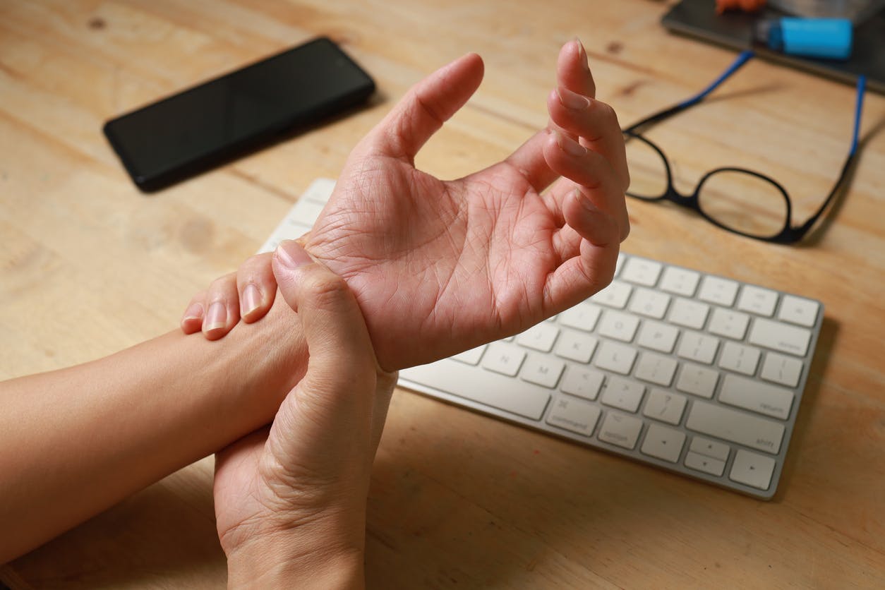person holding their wrist with keyboard in background