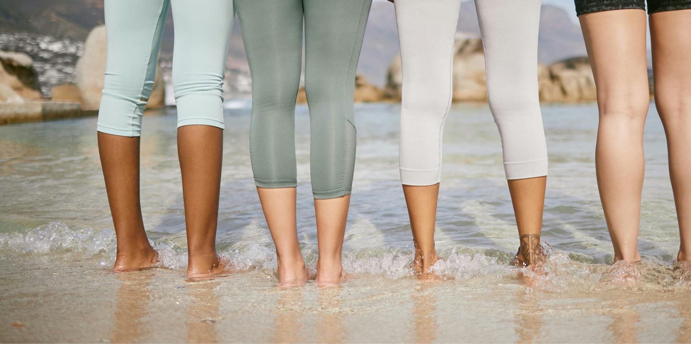 womens legs as they stand on the beach with their feet in the water