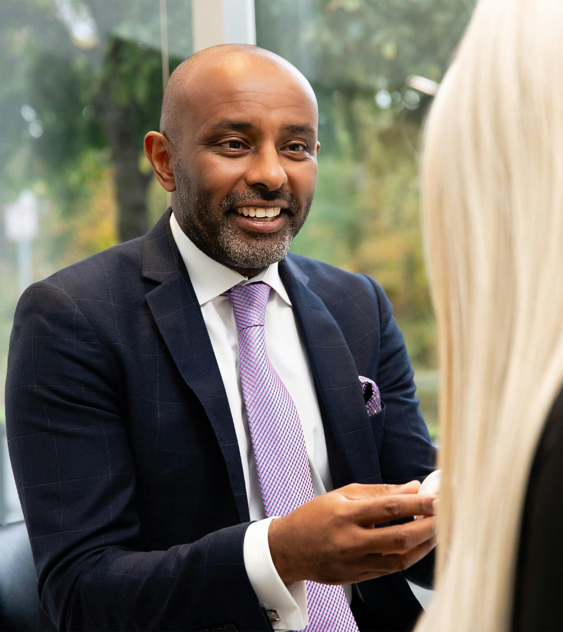 Man in a suit smiling at someone with blonde hair