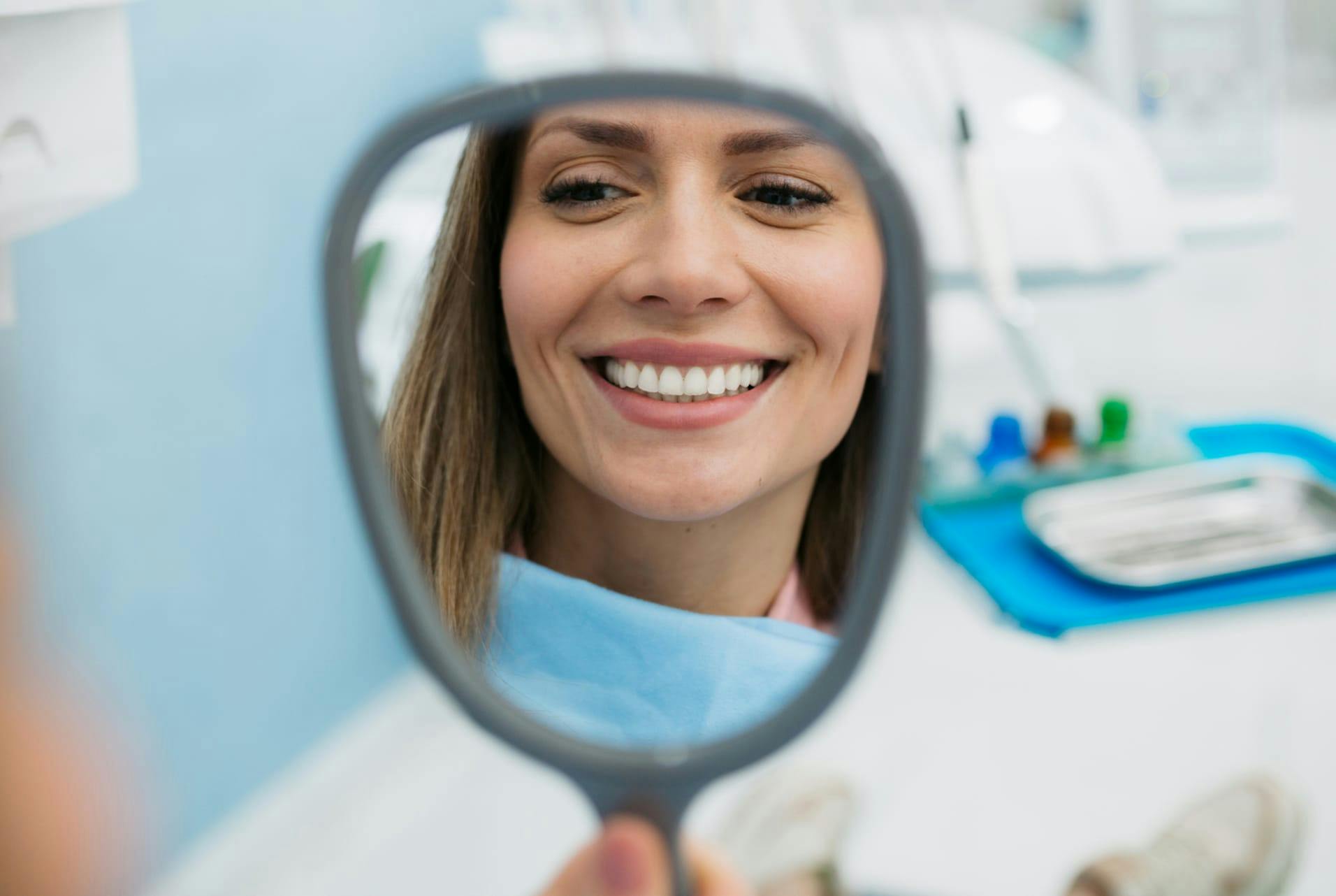 woman smiling looking at a handheld mirror