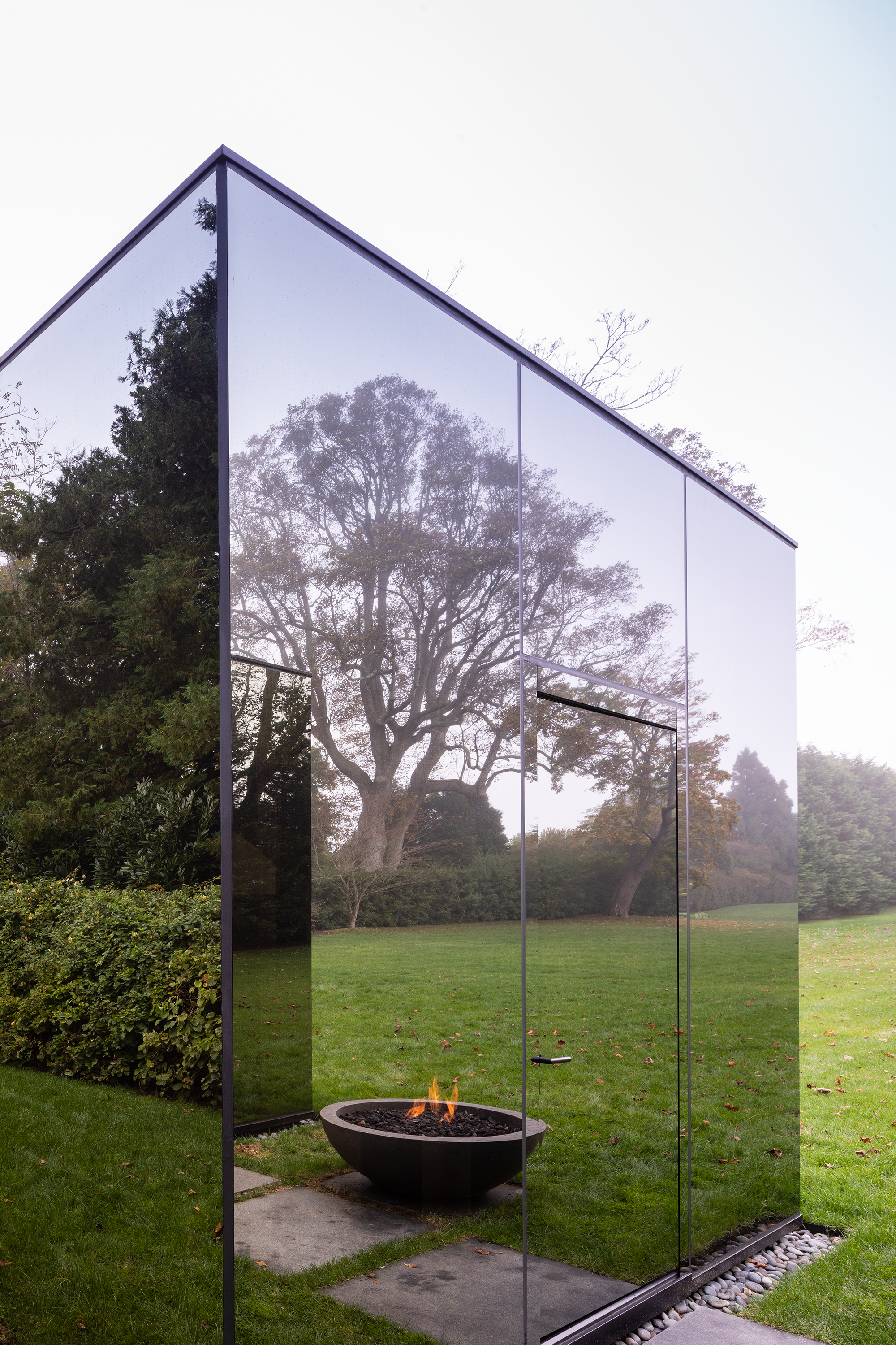 Photo of a mirrored build reflecting a grass lawn and fire pit