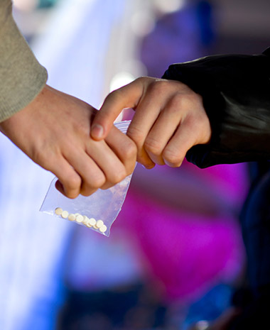 Two sets of hands exchanging a bag with pills in it.