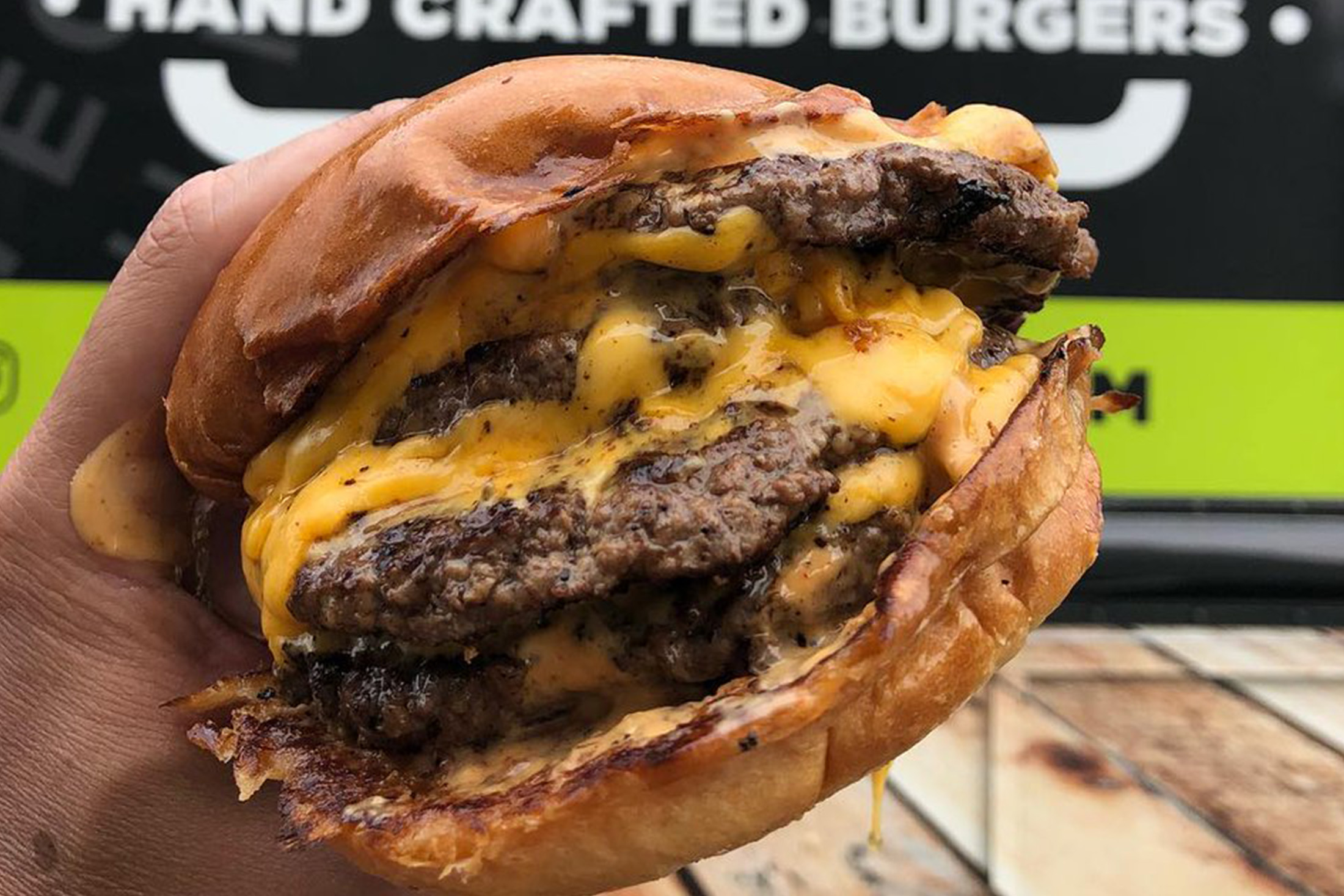 A hand holding a very large cheeseburger.