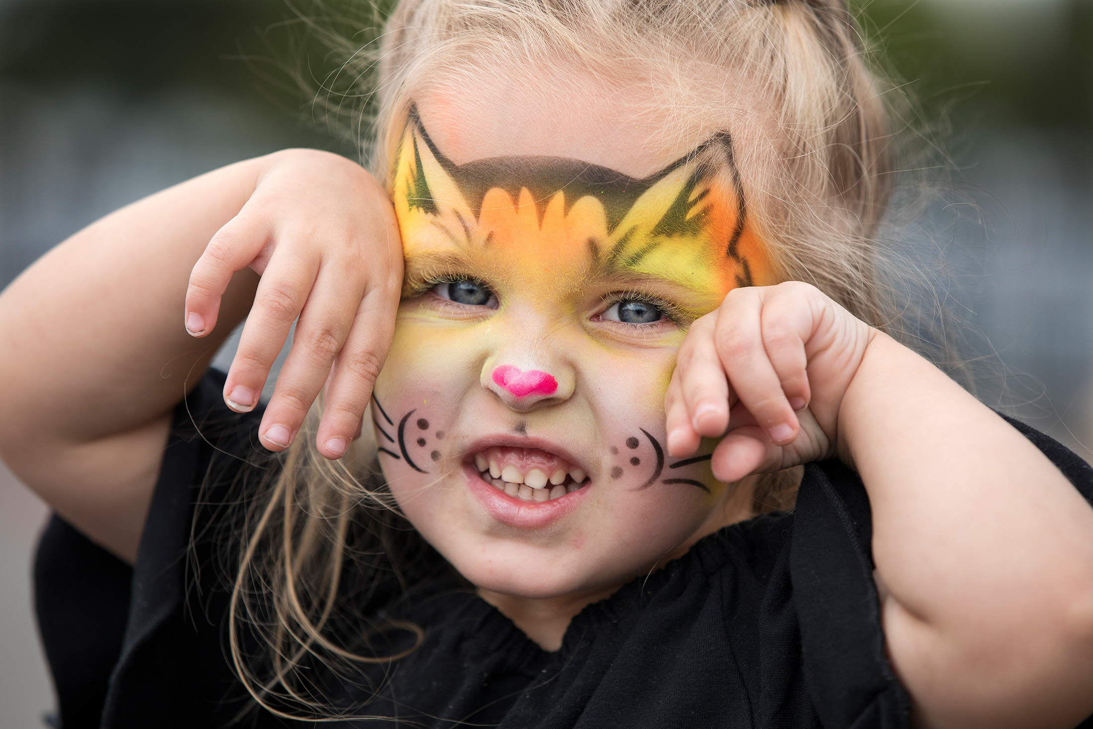A small child with their face painted as a cat, complete with ears and whiskers.