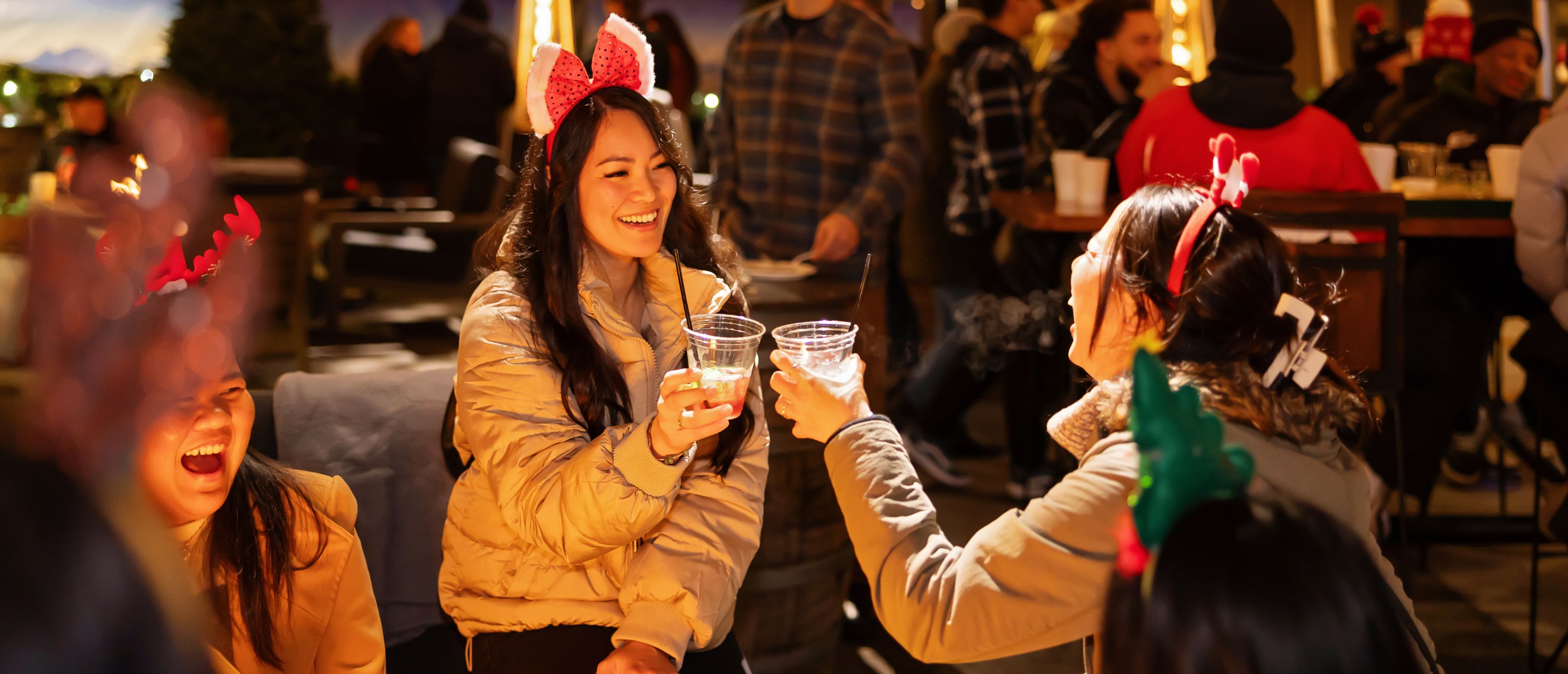 Friends wearing festive holiday headbands toast their drinks with smiles on their faces in the YETI Bar at Holiday Magic.