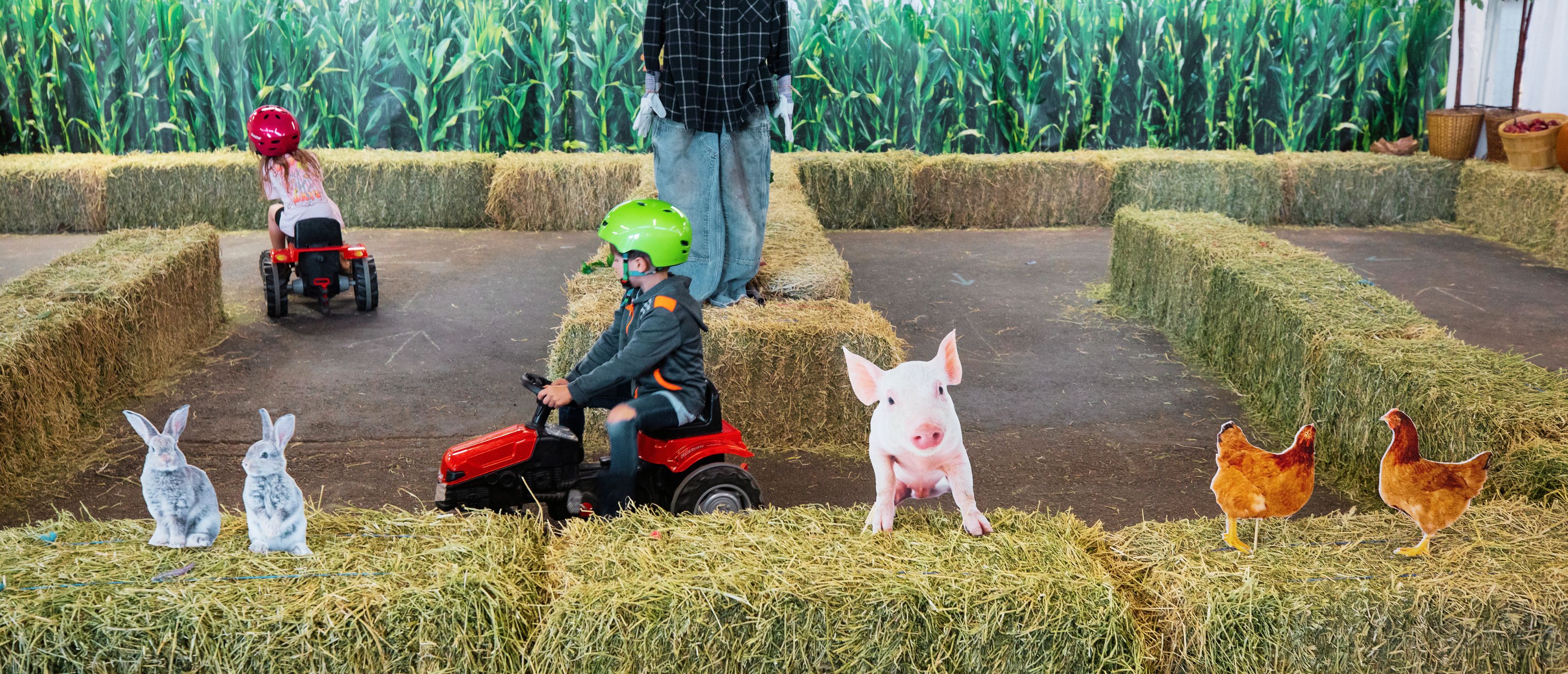 Two kids riding pedal tractors in hay bale maze at Wheels on the Farm