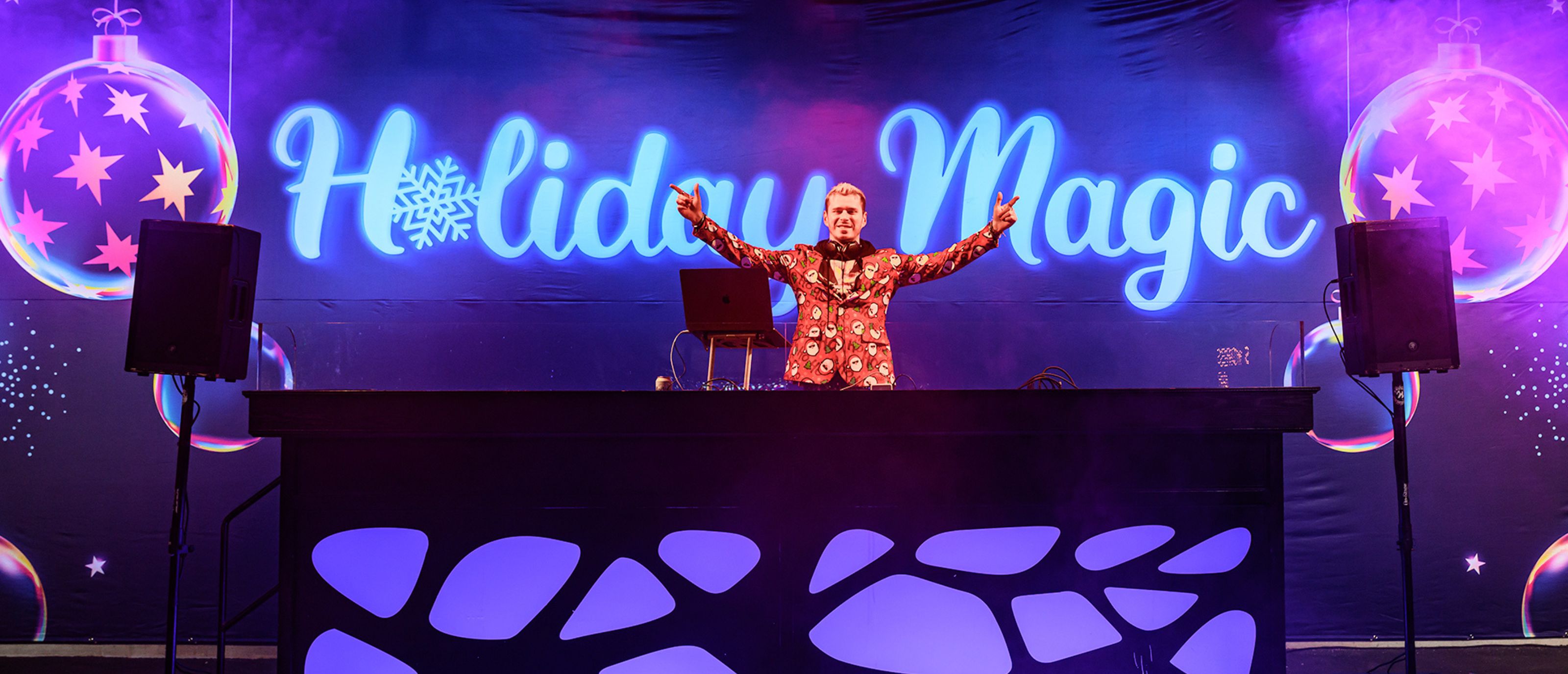 DJ with arms out on stage in front of Holiday Magic backdrop