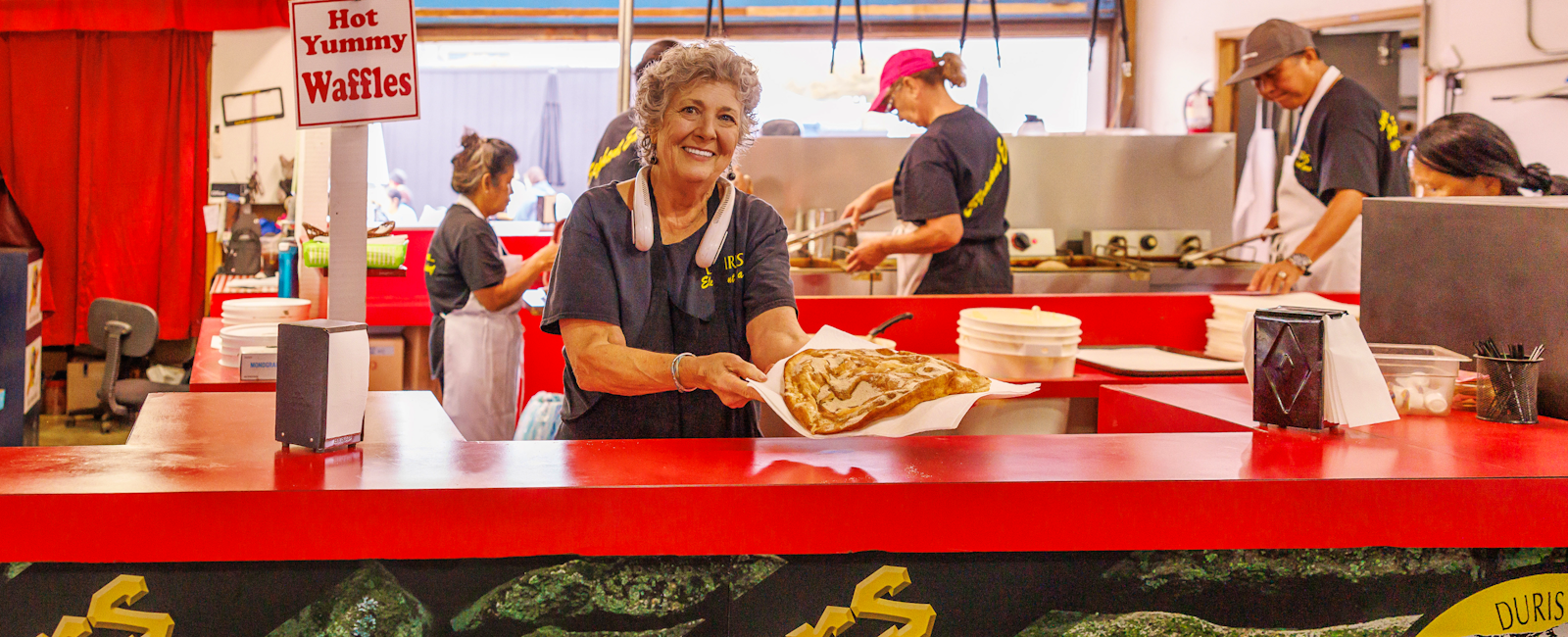 Women working at Duris Elephant Ear booth holding out elephant ear to the camera