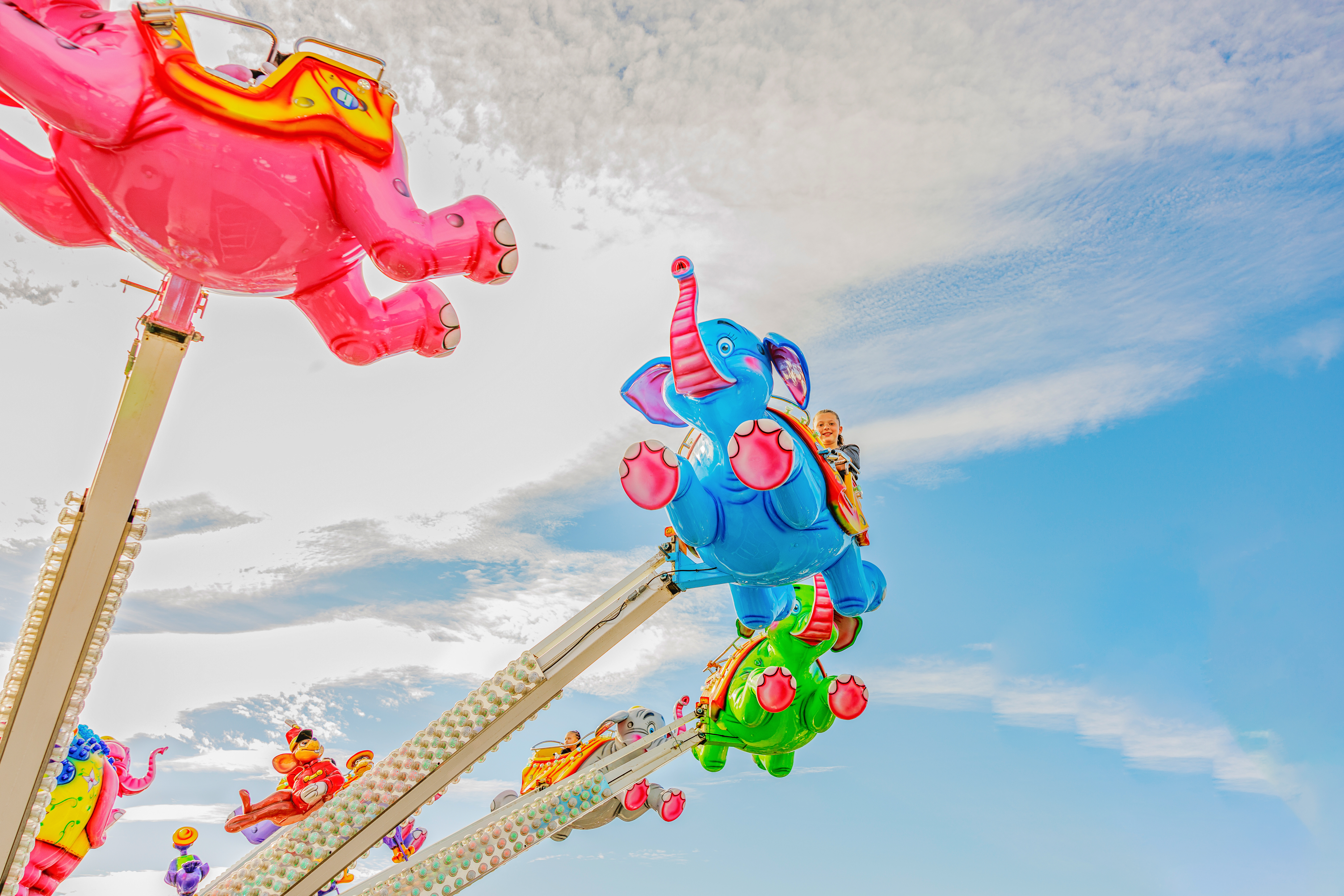 A ride with multicolored flying elephants and a blue sky with white clouds above
